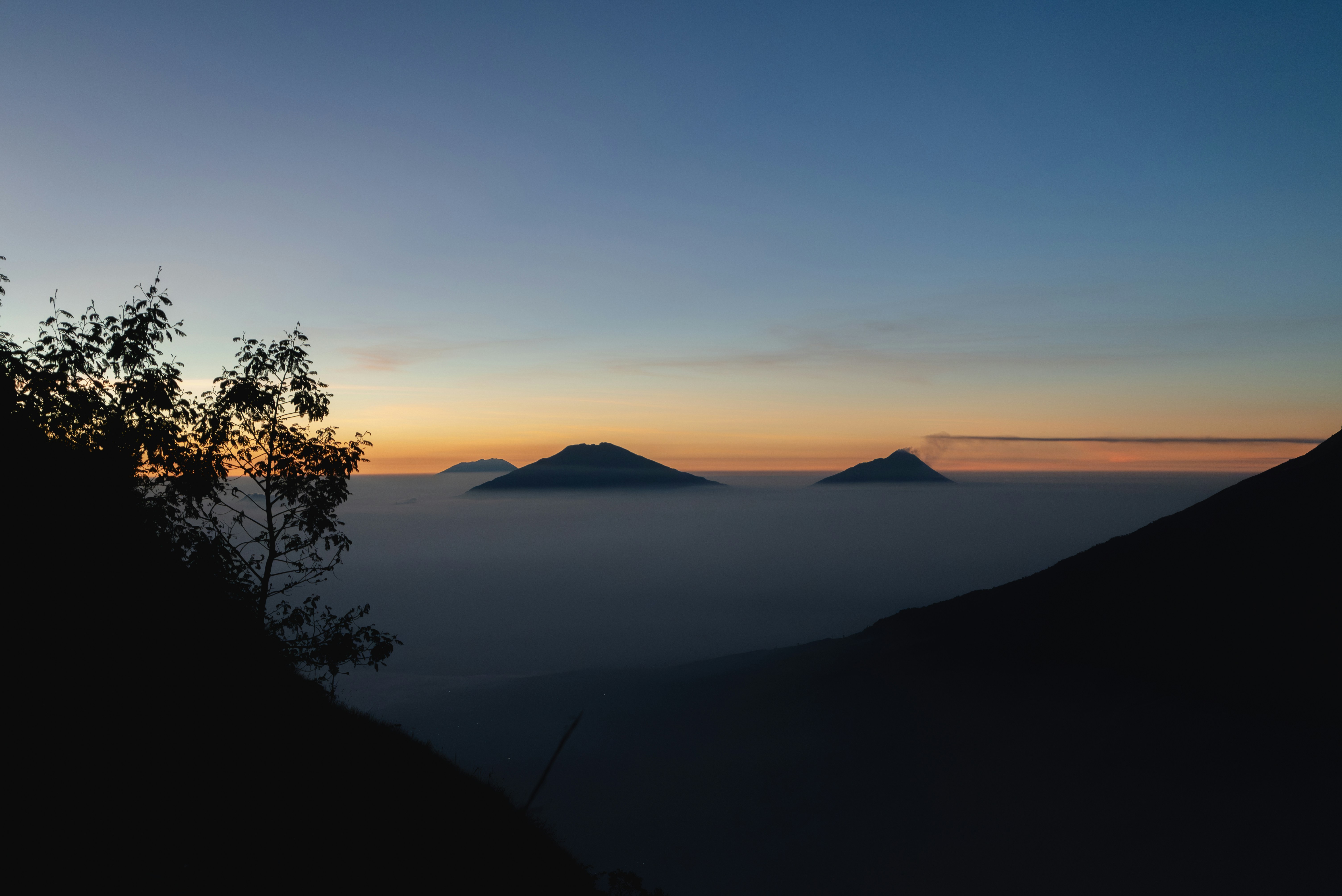 Volcanic peaks rising above a thick layer of low clouds at golden hour