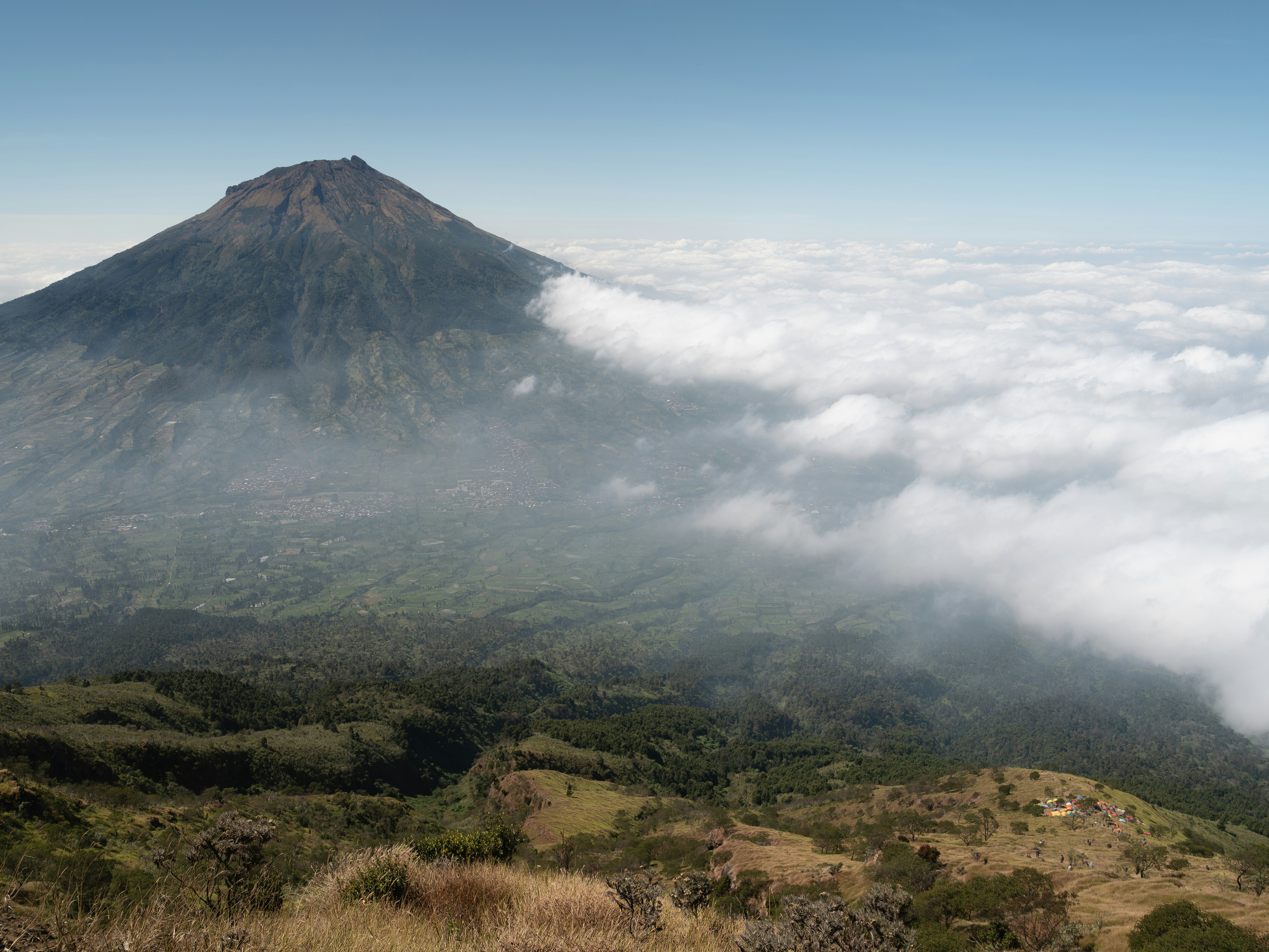 A large volcanic mountain rising above a valley filled with clouds and green fields