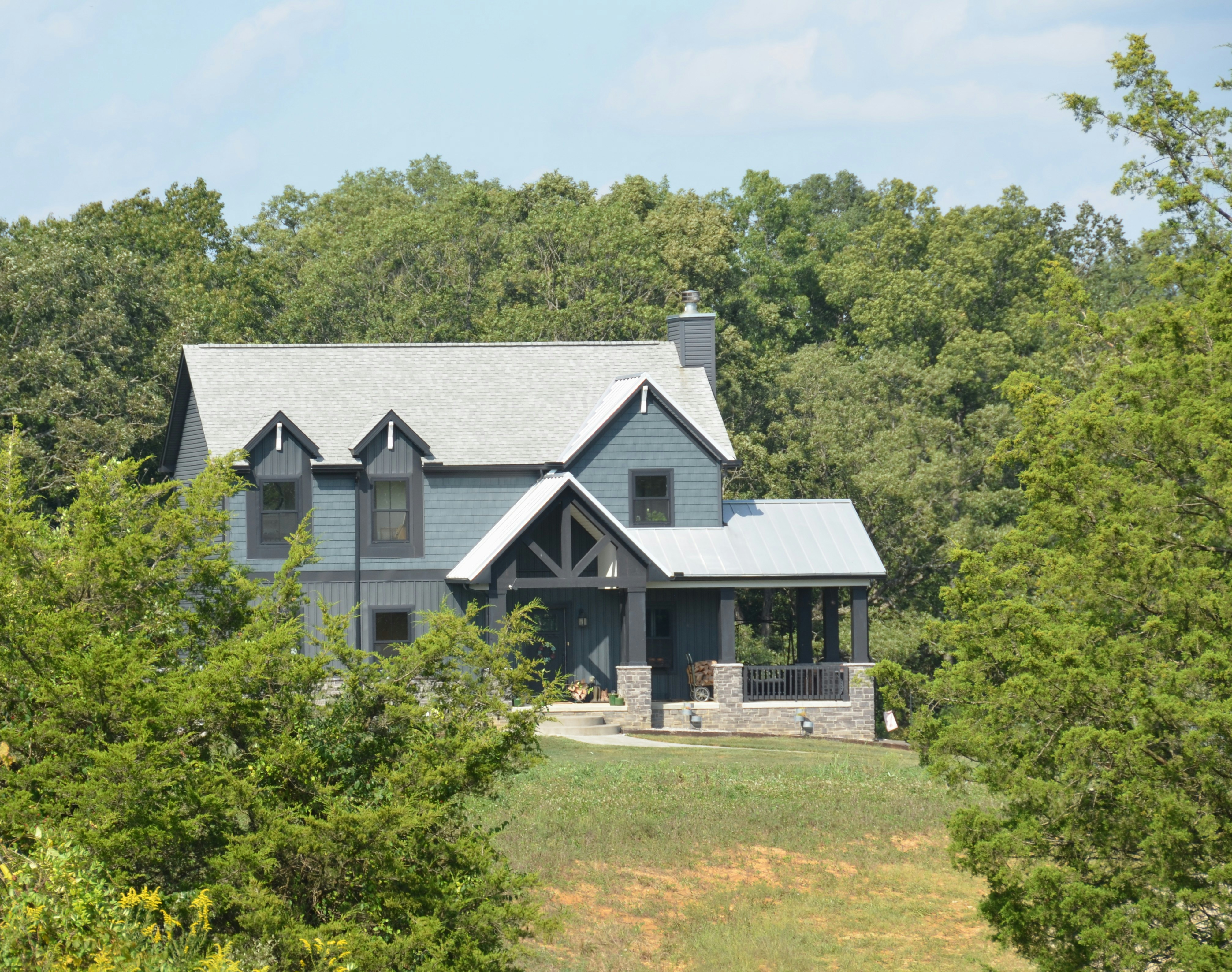 Blue house with a gray roof surrounded by tall green trees