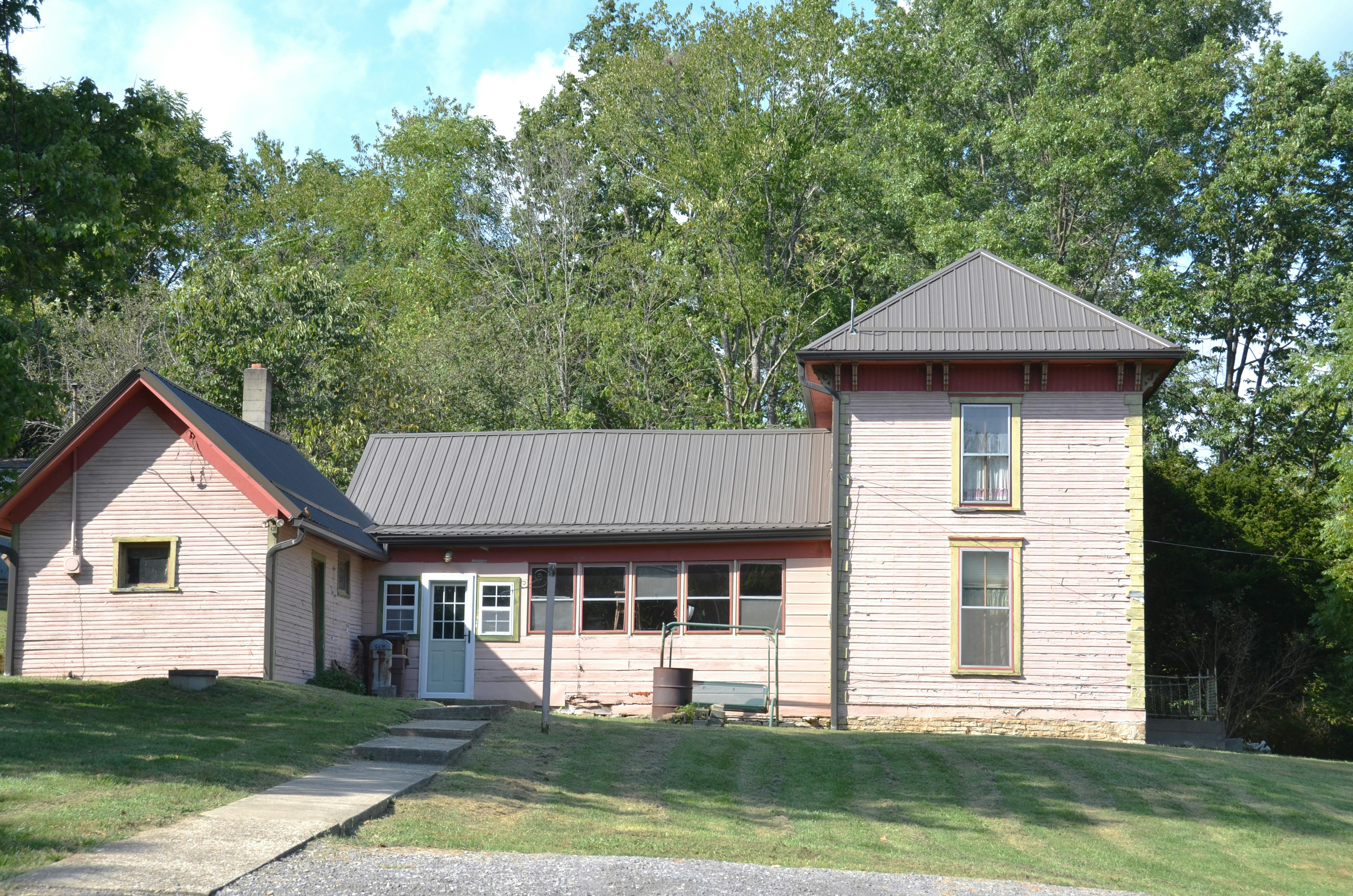 A pink wooden house with a metal roof and green trim in a yard