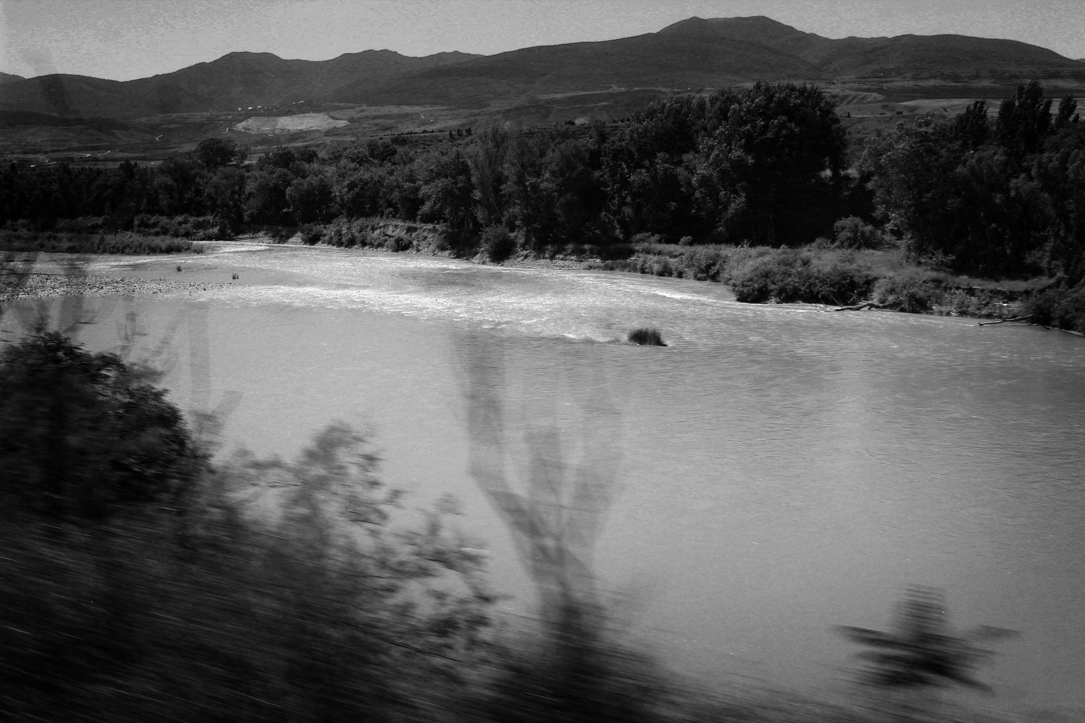 Un río ancho que fluye entre árboles y montañas lejanas en blanco y negro