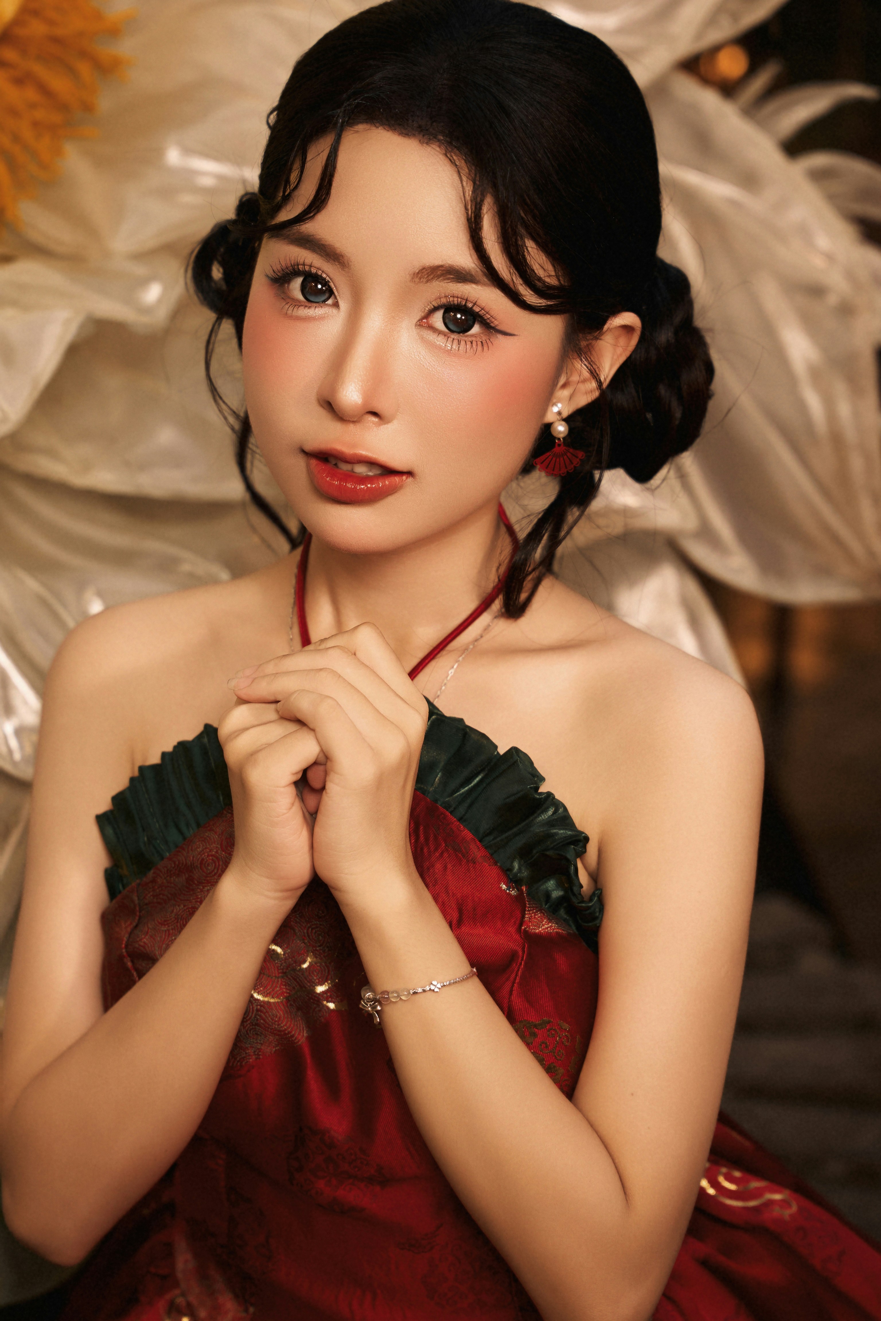 A woman in a red and green halter dress with hands clasped together