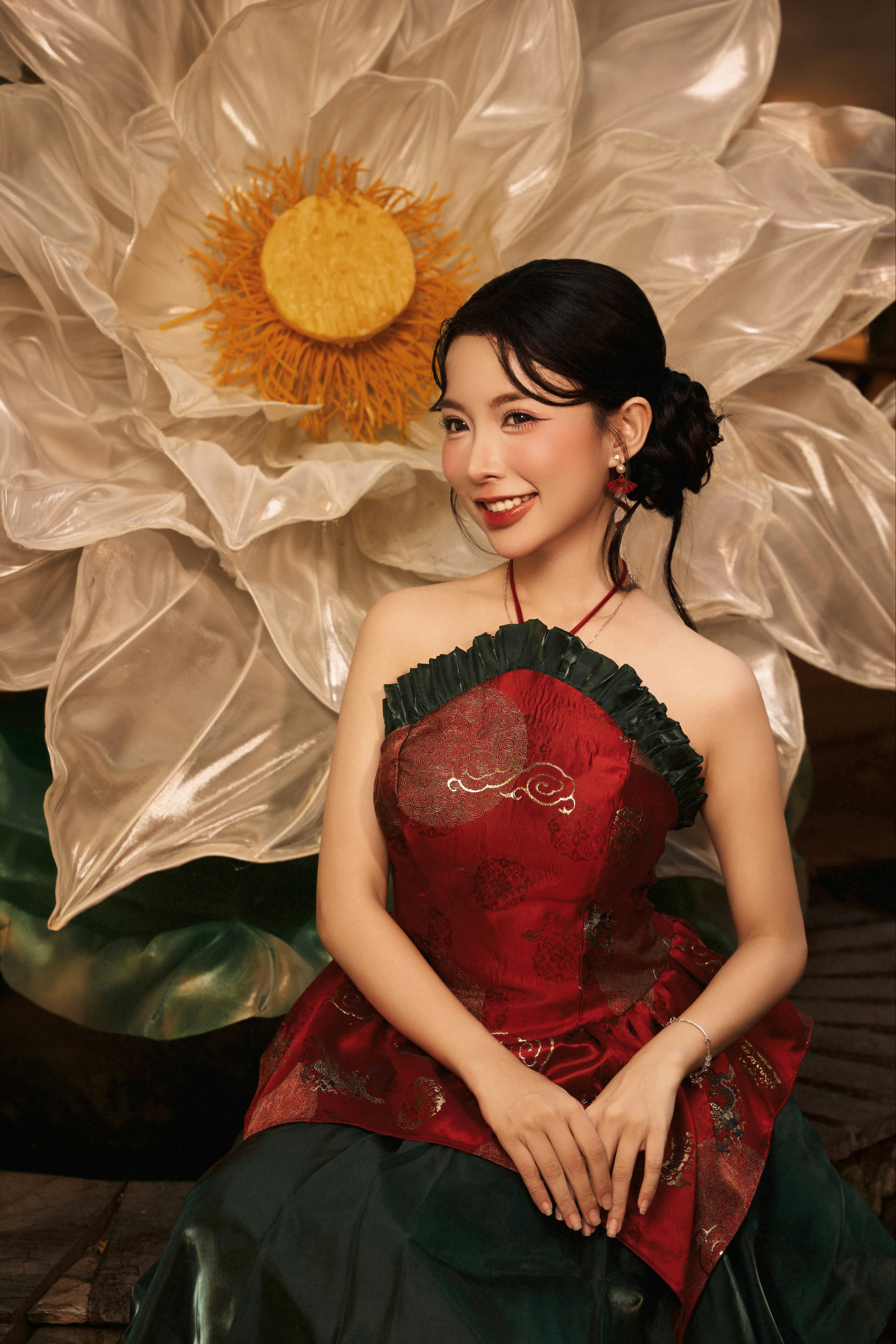 A woman in a red and green dress before a large white lotus flower