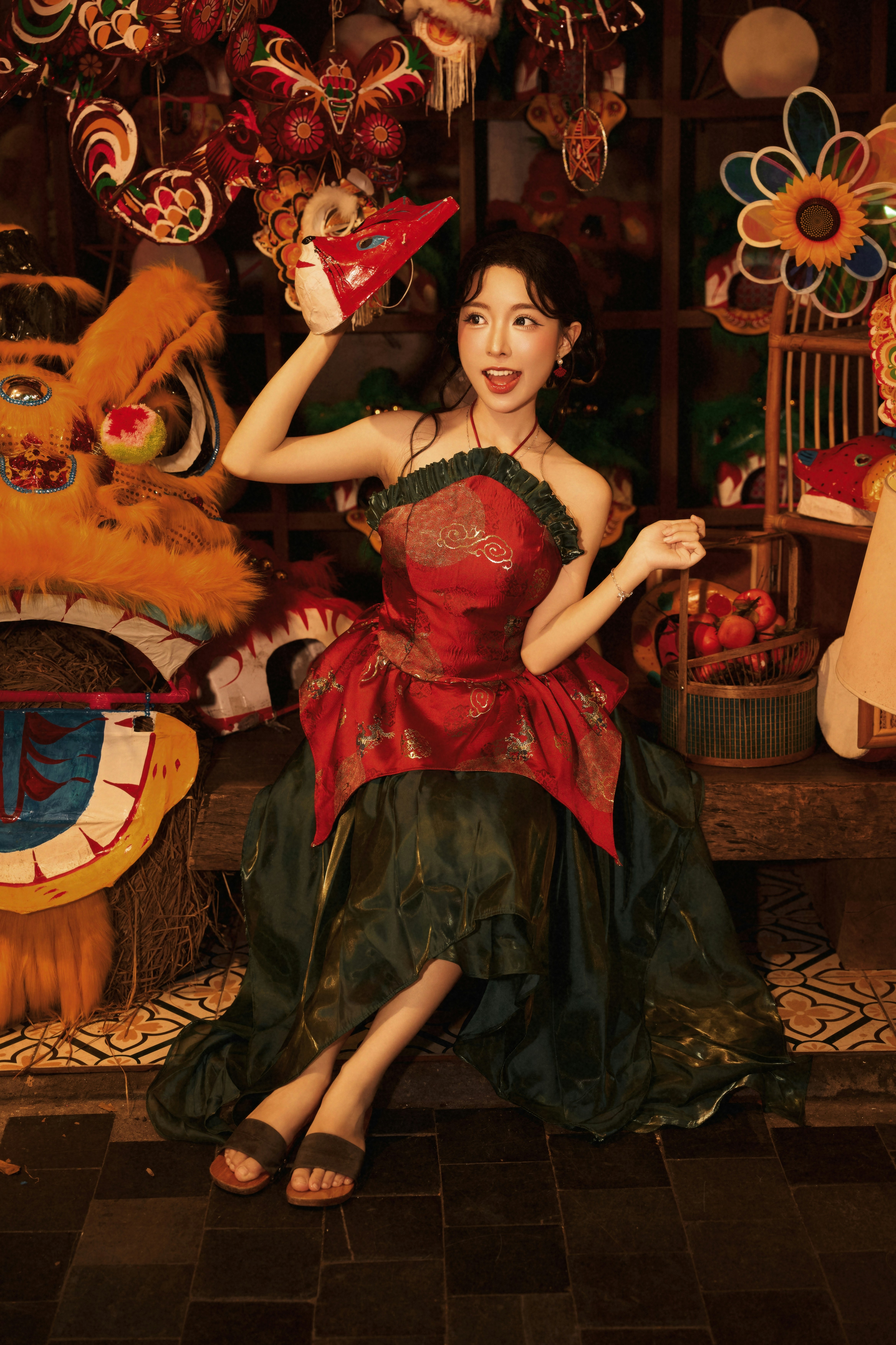 A woman in a red and green dress holding a mask near lion dance props