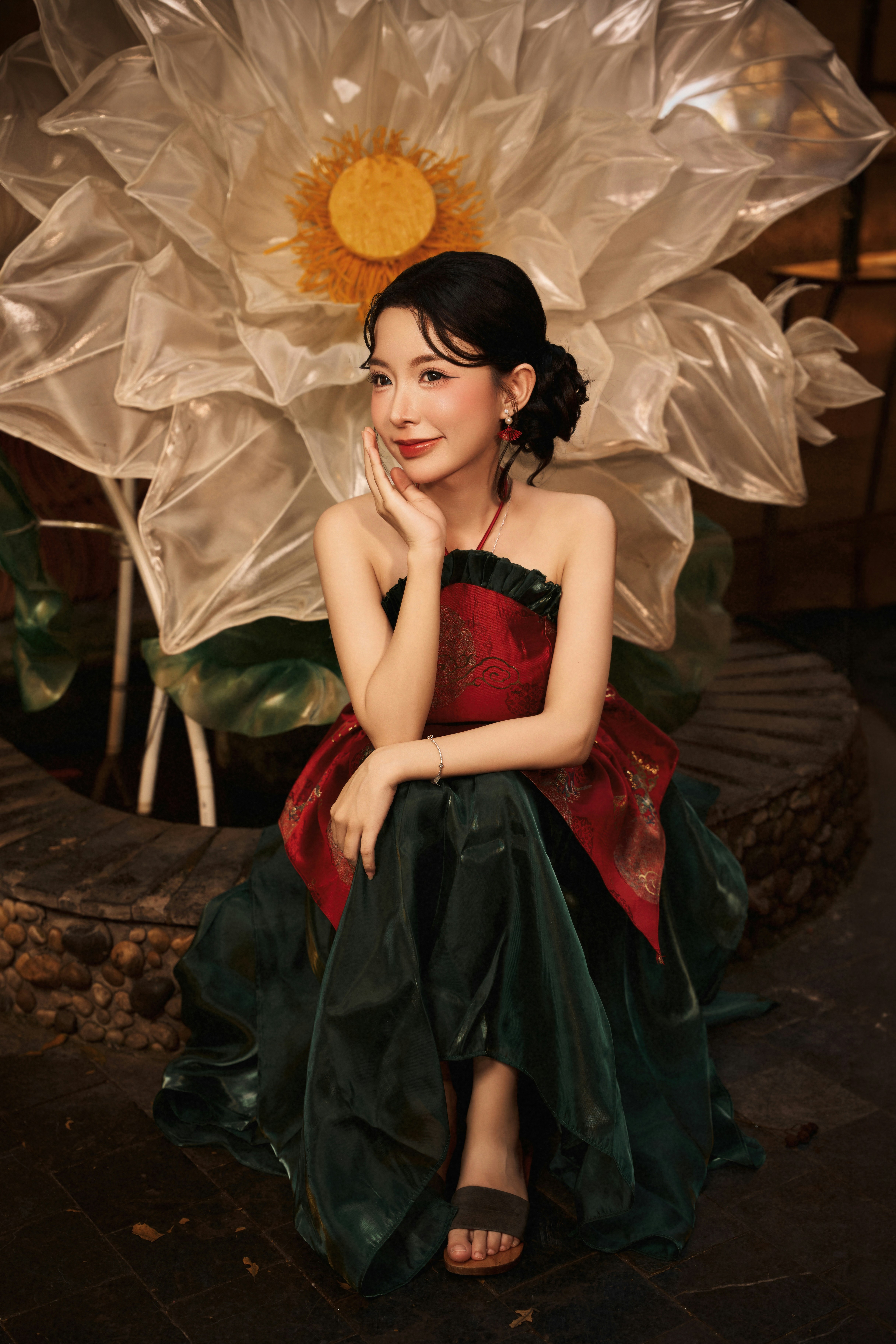 A woman in a red and green dress sitting before a large white lotus