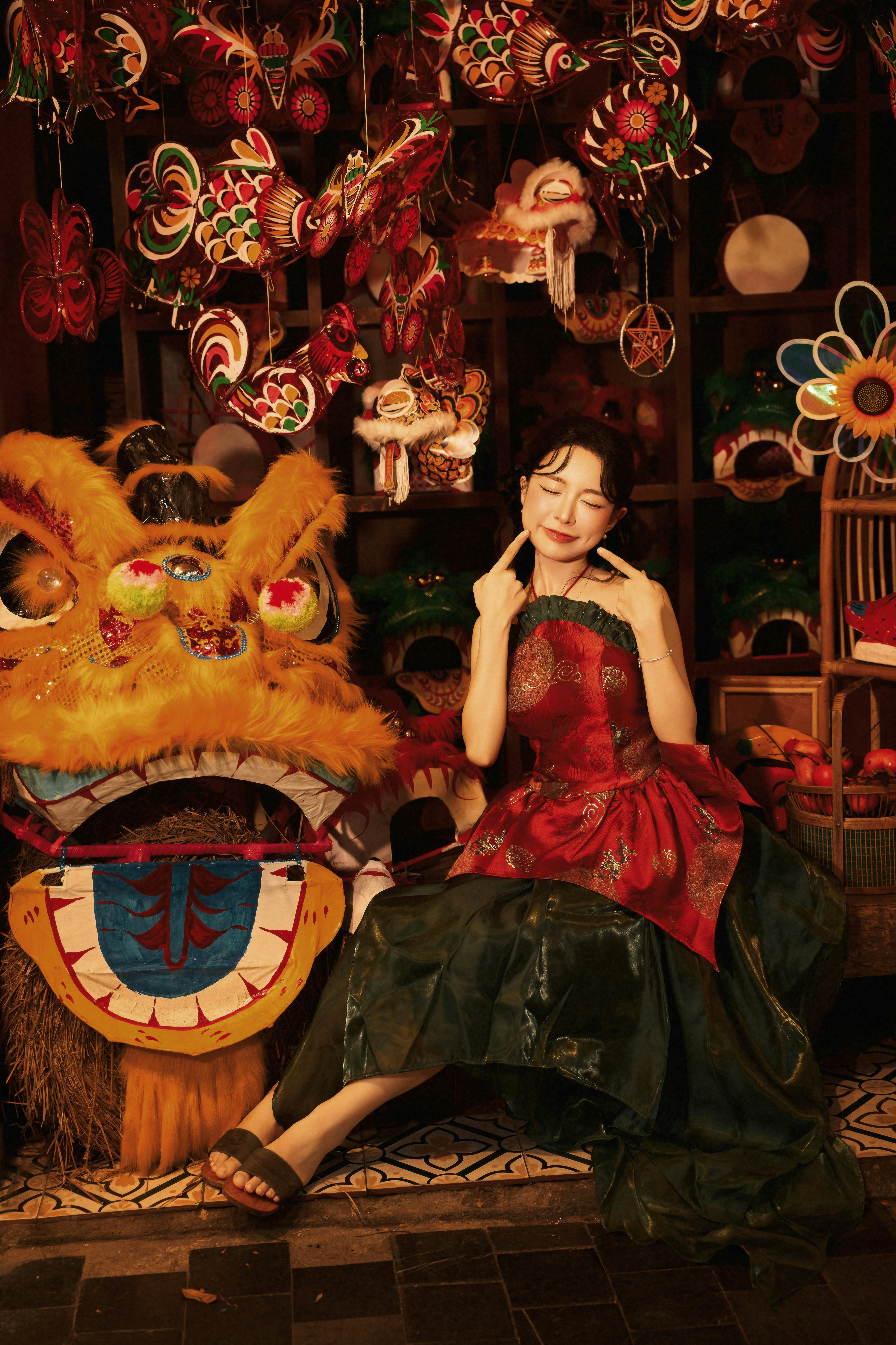 A woman in a red and green dress beside a large lion dance head
