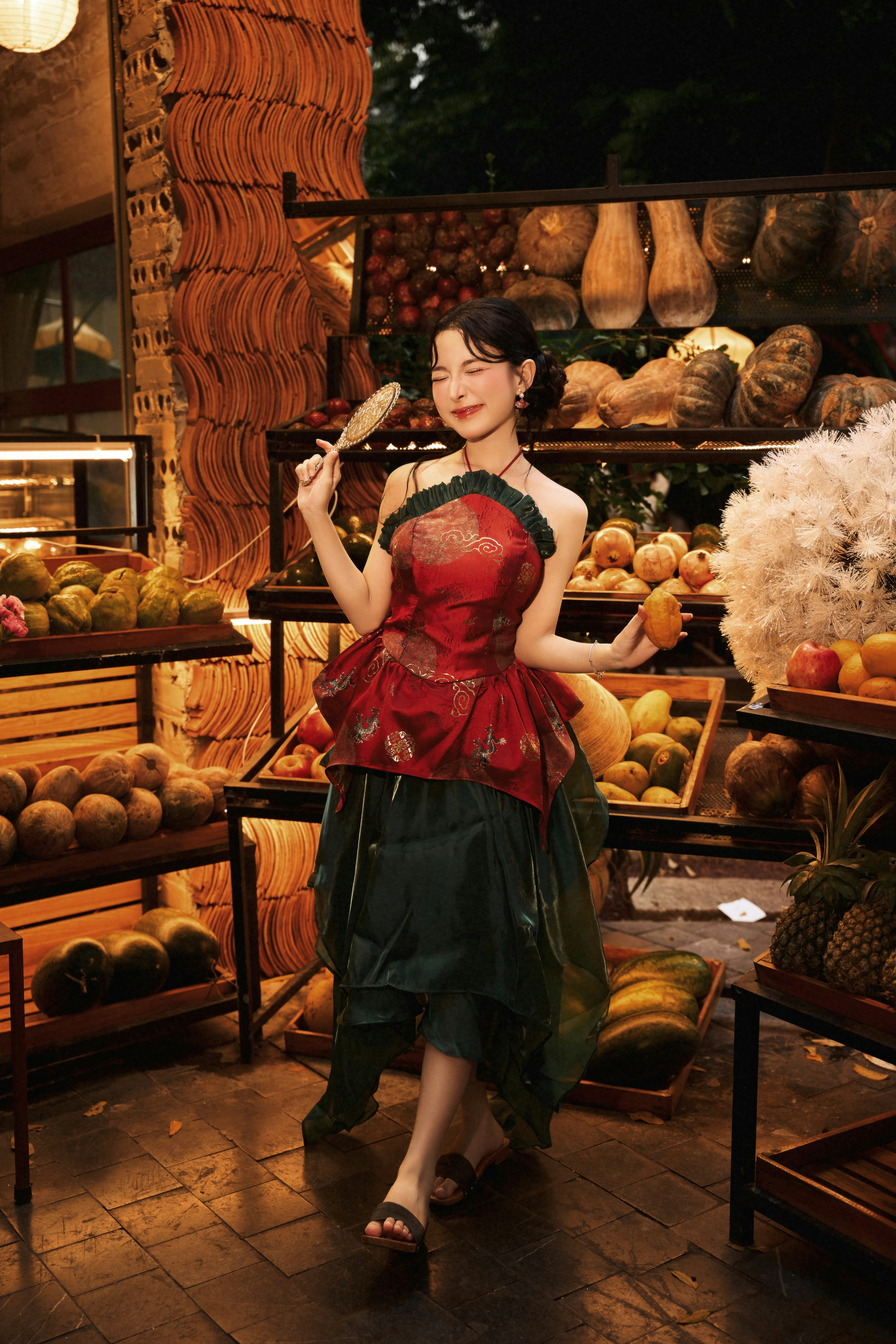 A woman in a red and green dress holding a mirror in a fruit market