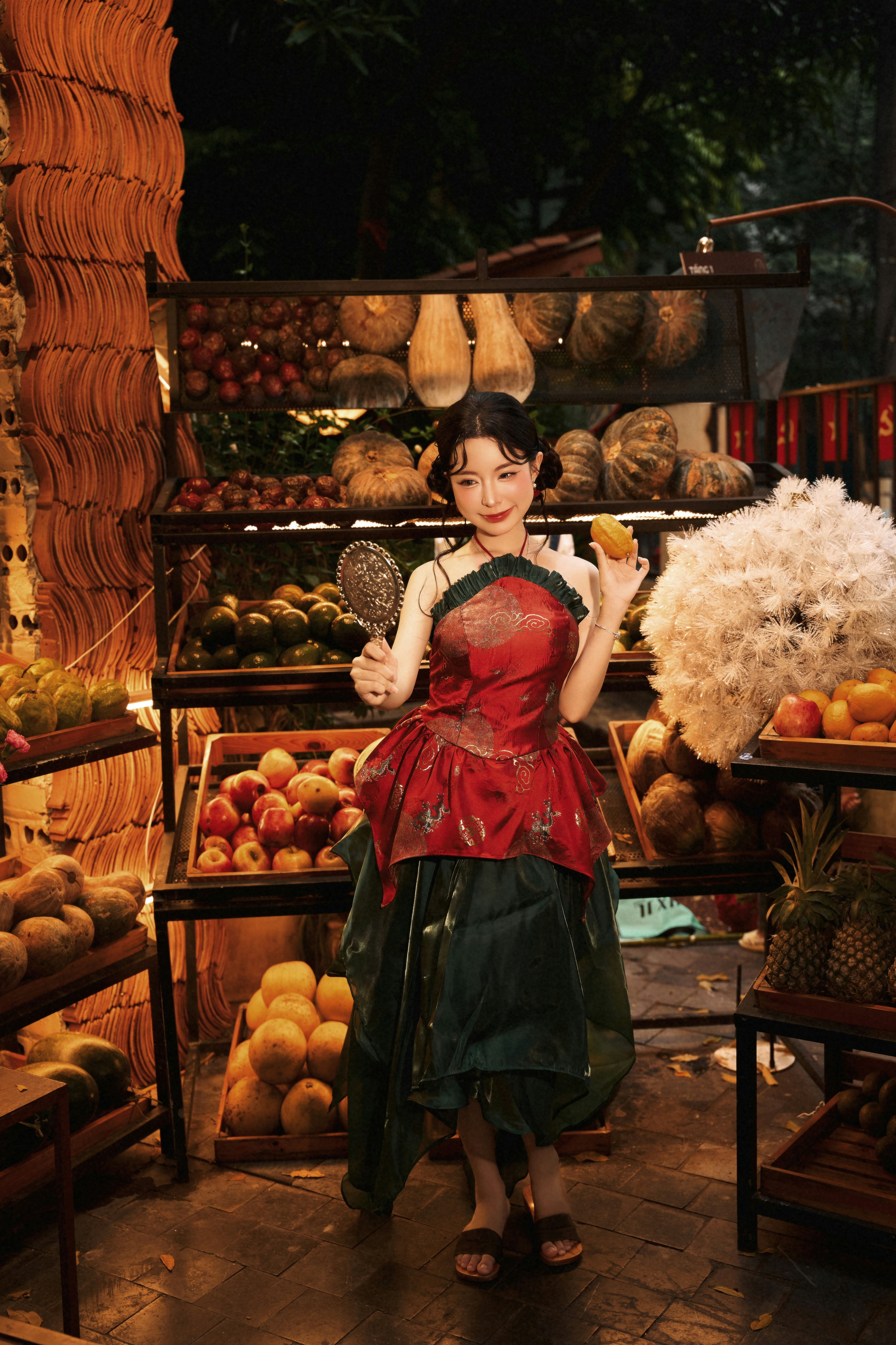 A woman in a red and green dress holding a mirror and fruit