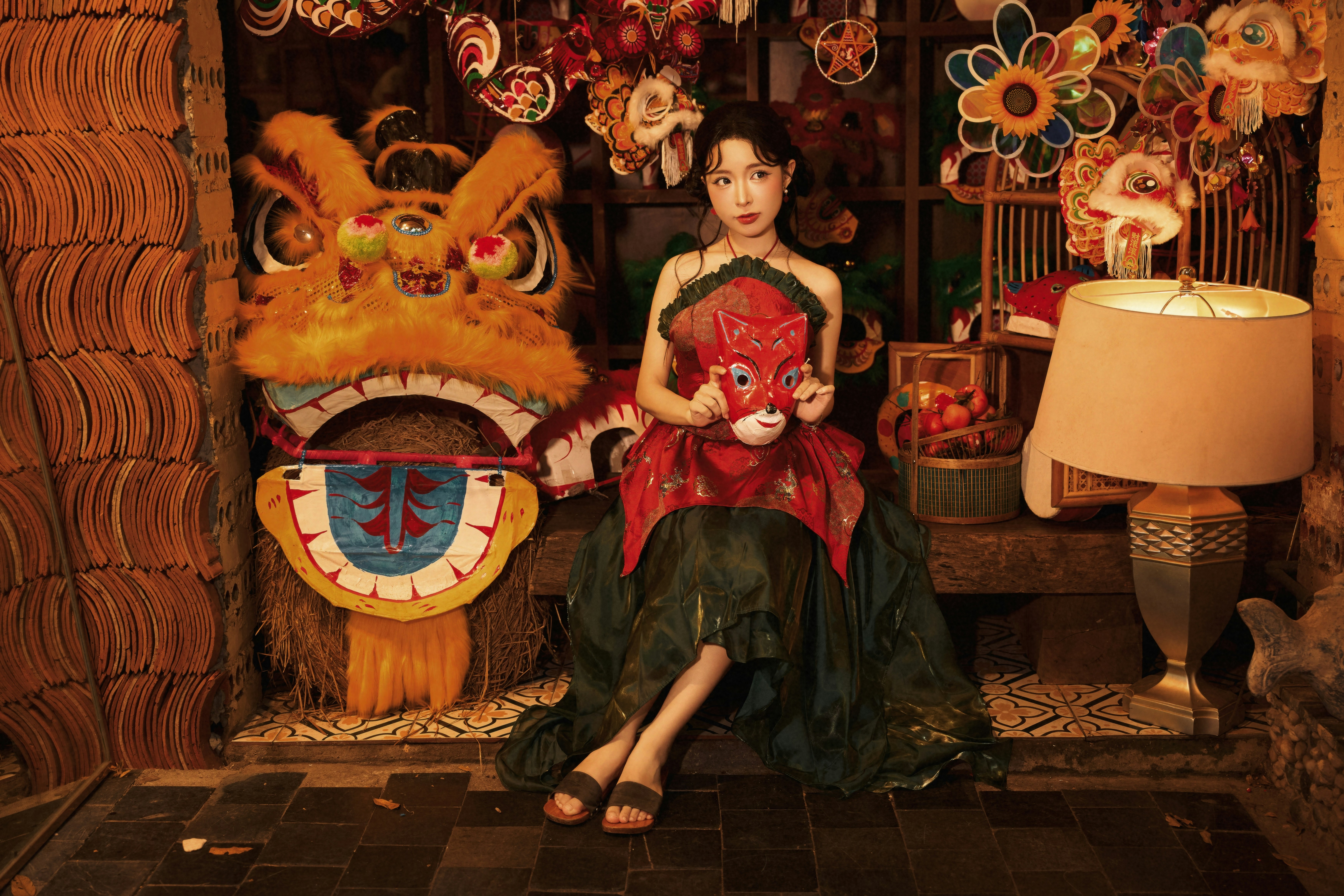 A woman holding a red mask amidst dragon heads and lanterns in a festive shop