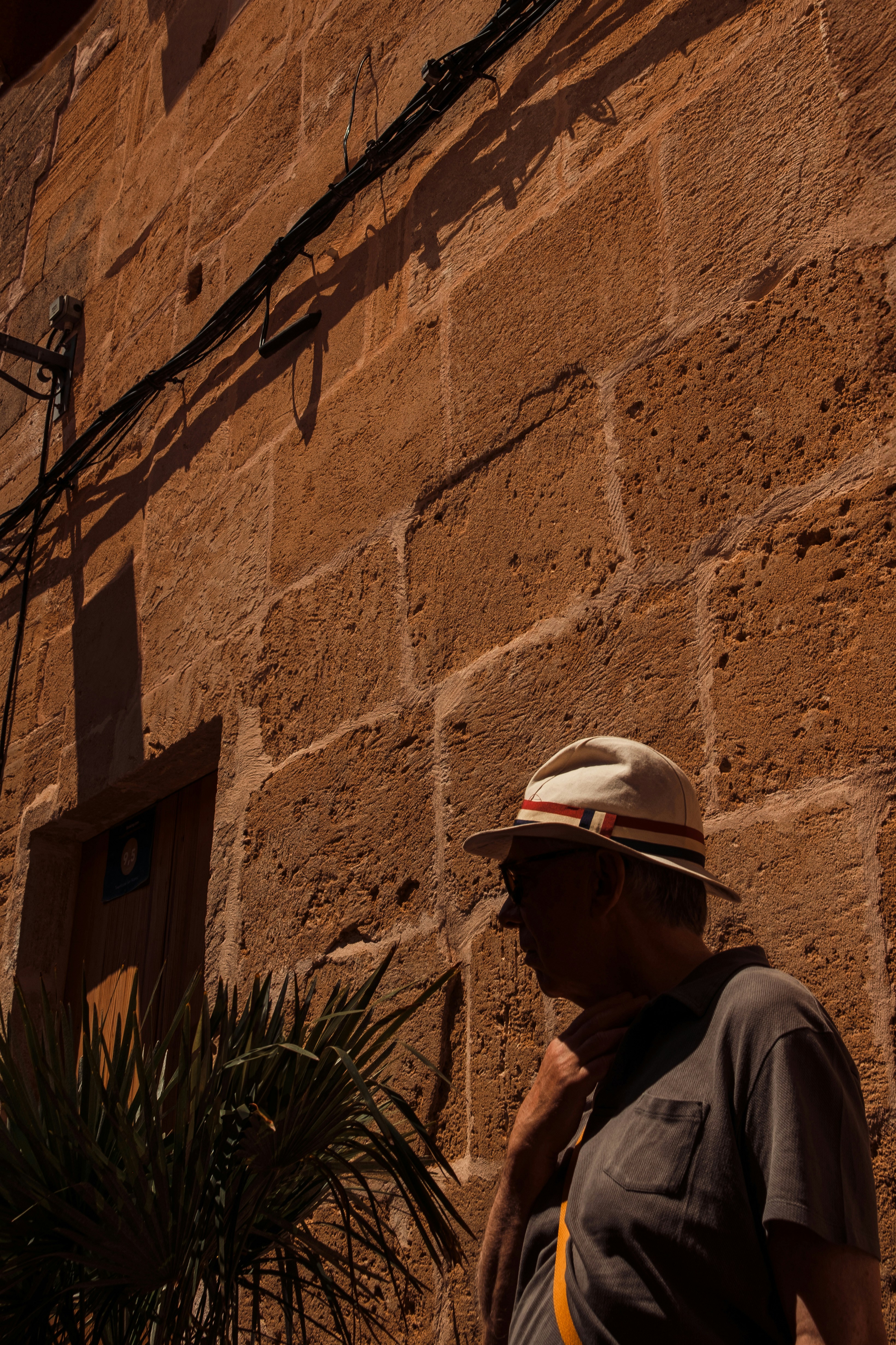 A person in a hat and grey shirt against a textured stone wall