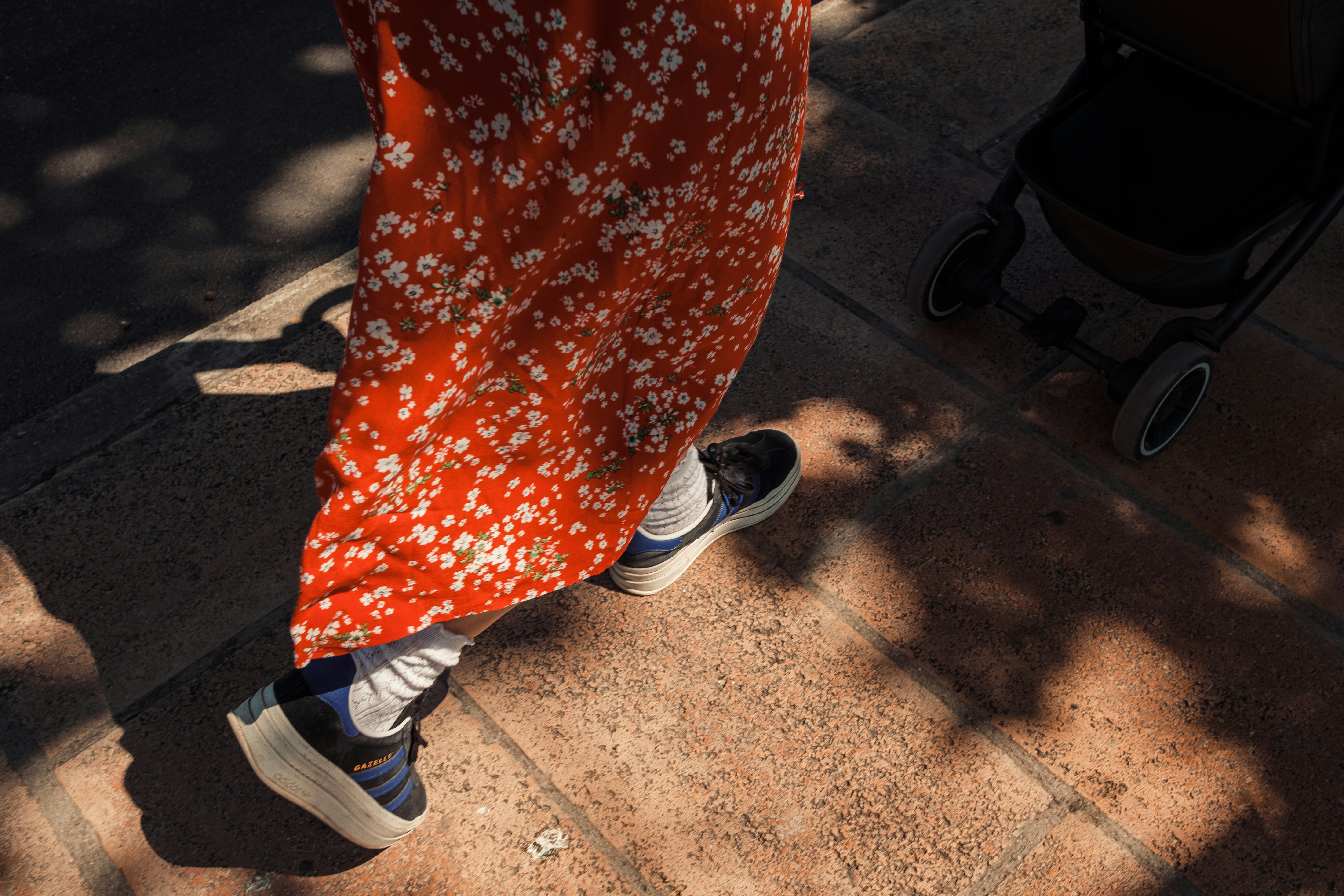A person in a floral red dress and sneakers walking beside a stroller