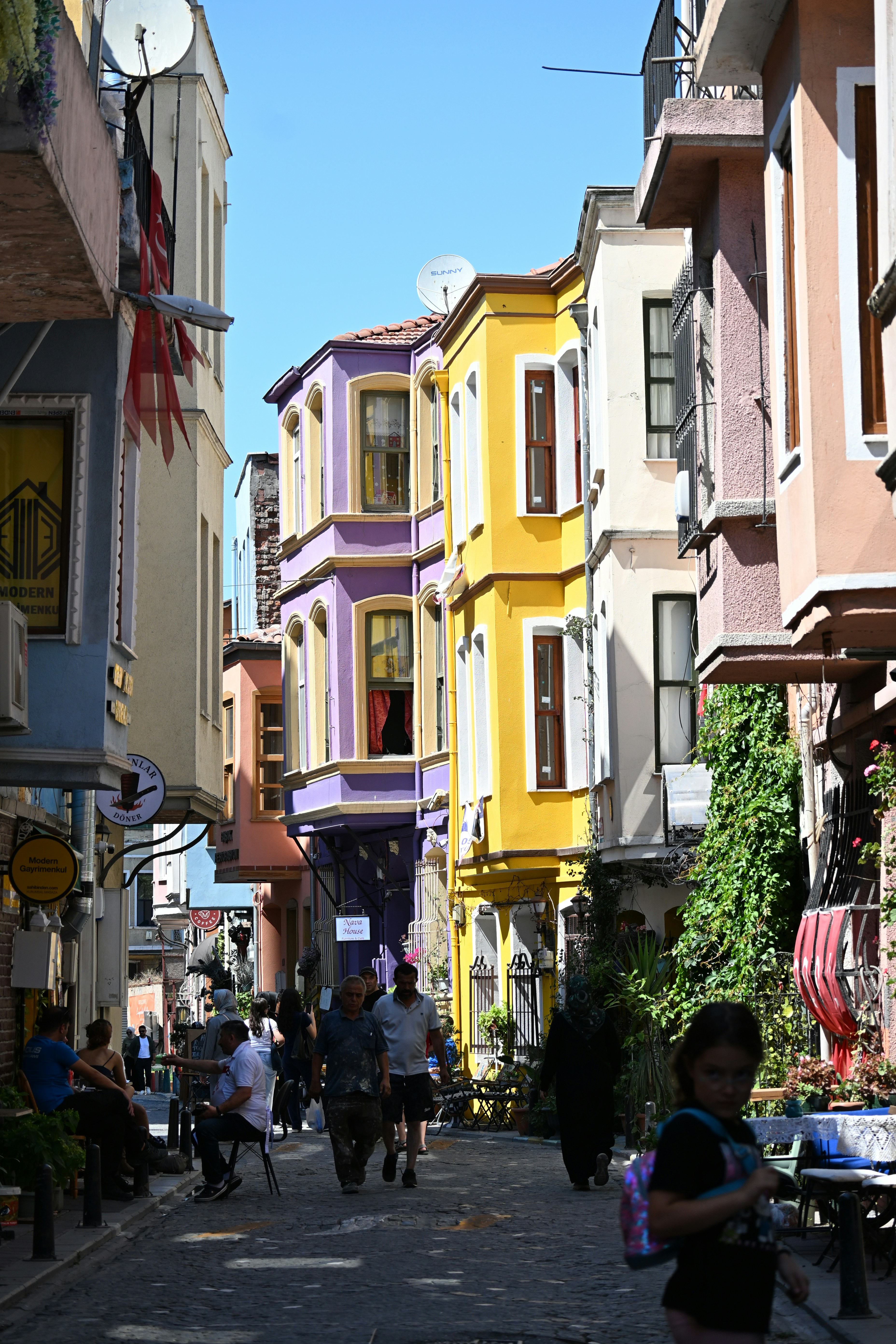 Gente caminando por una estrecha calle empedrada bordeada de edificios coloridos en amarillo y morado