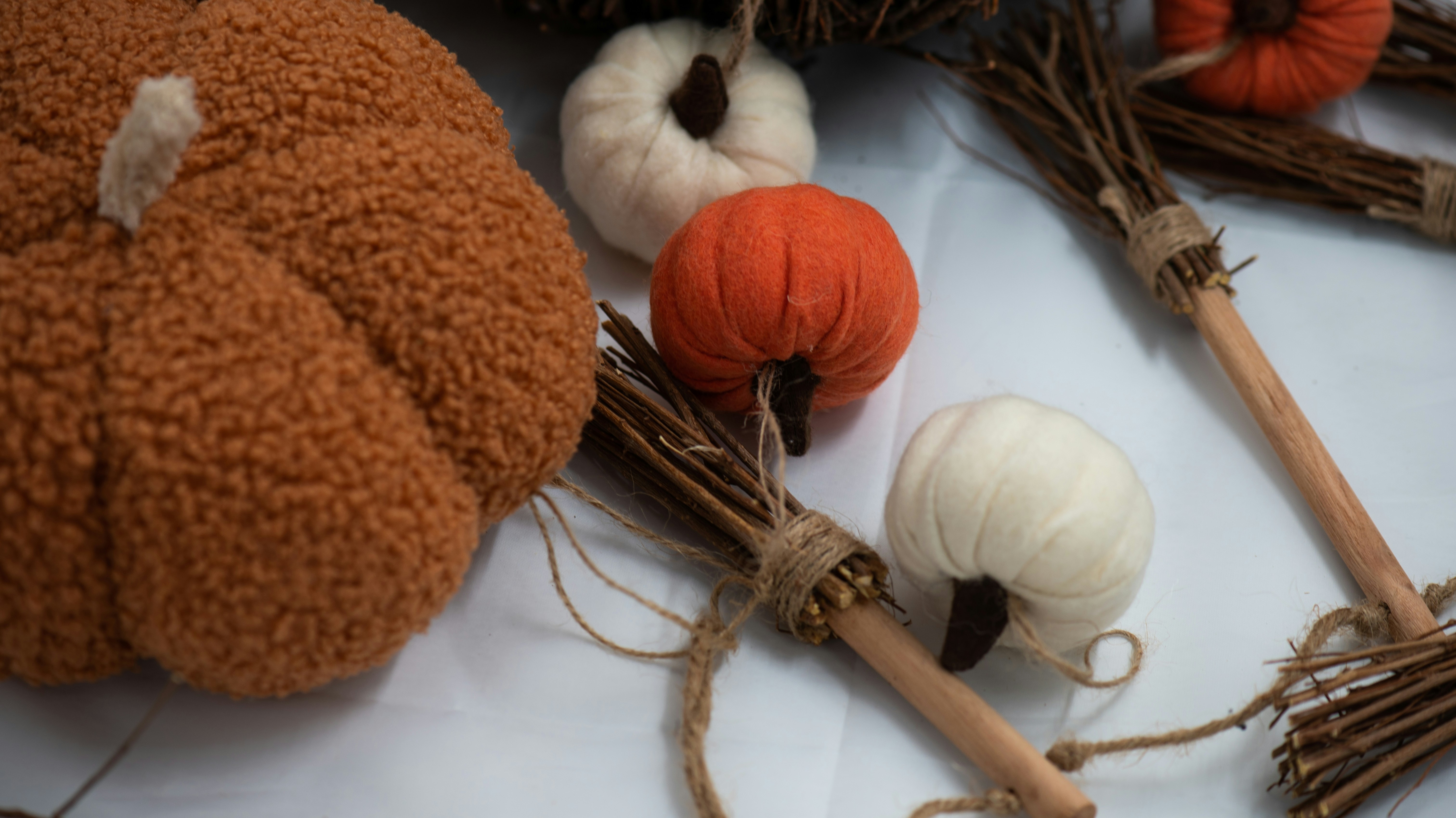Fabric pumpkins and miniature twig brooms arranged on a white surface