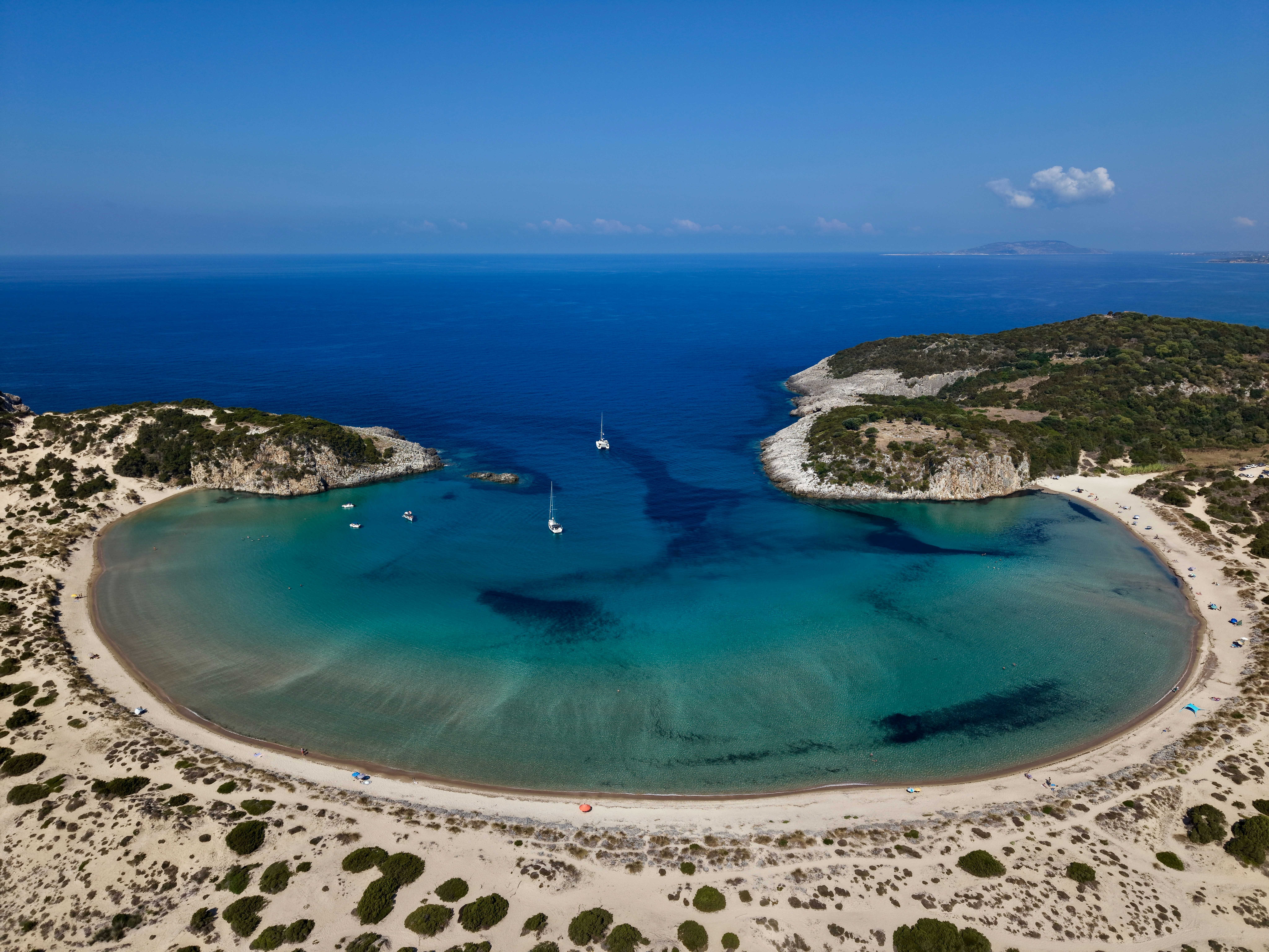Aerial view of a crescent-shaped beach with turquoise water and two sailboats
