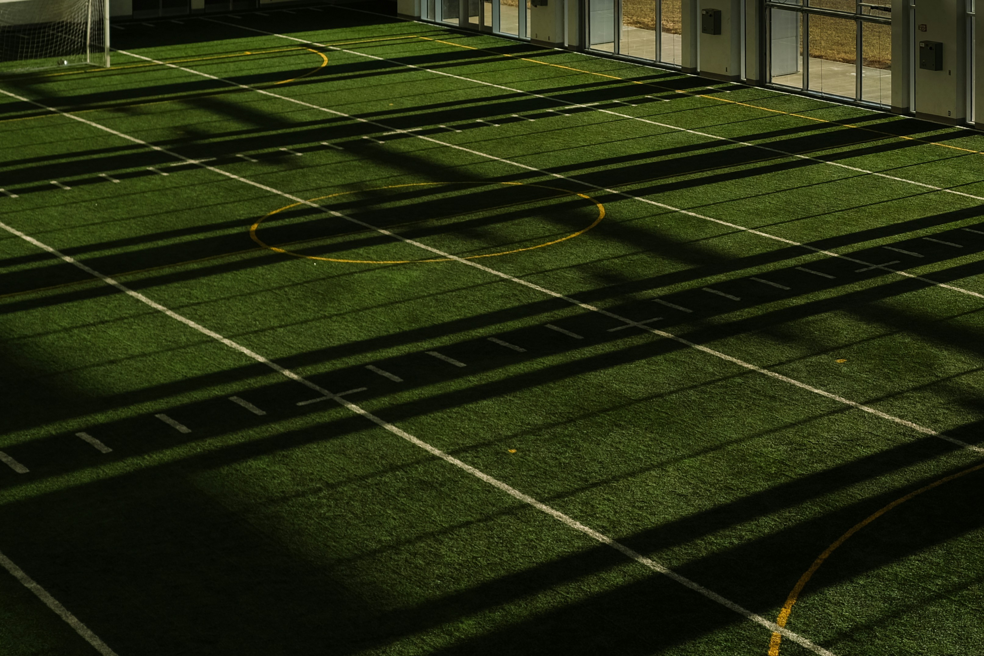 An indoor artificial turf field with white yard lines and yellow circles