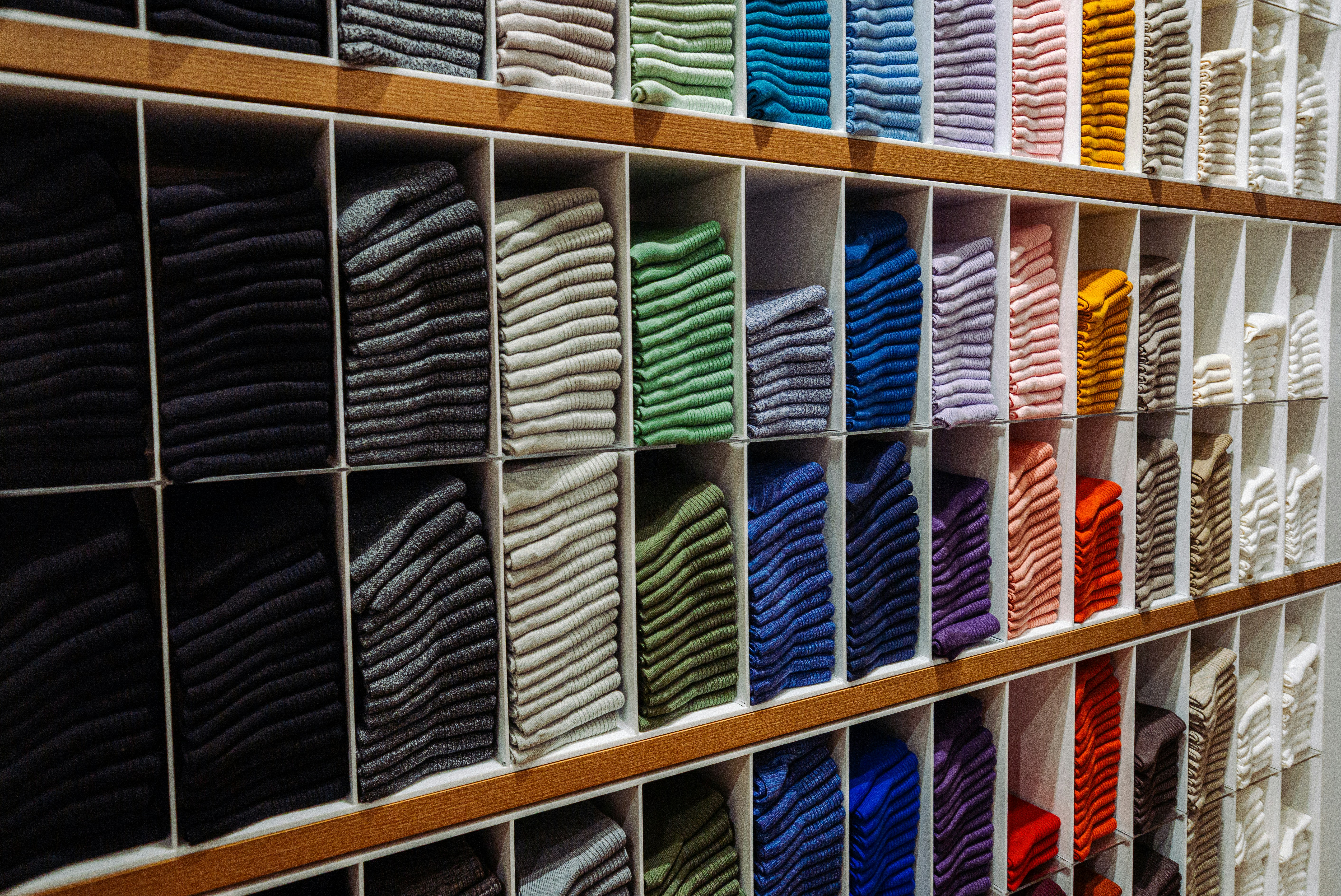 Stacks of folded colorful socks organized by shade on wooden retail store shelves