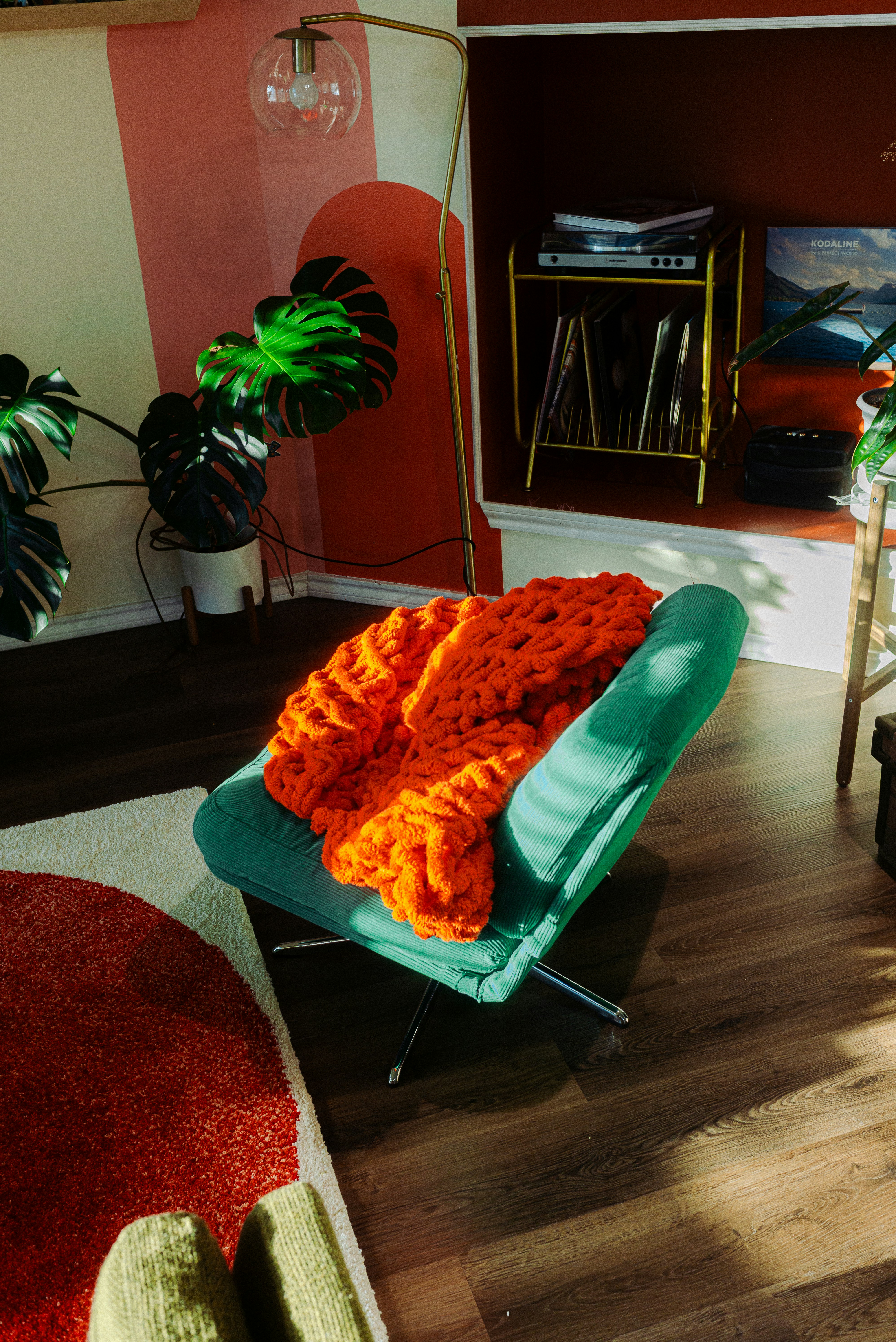A green corduroy armchair with a chunky orange knit blanket in a sunlit room