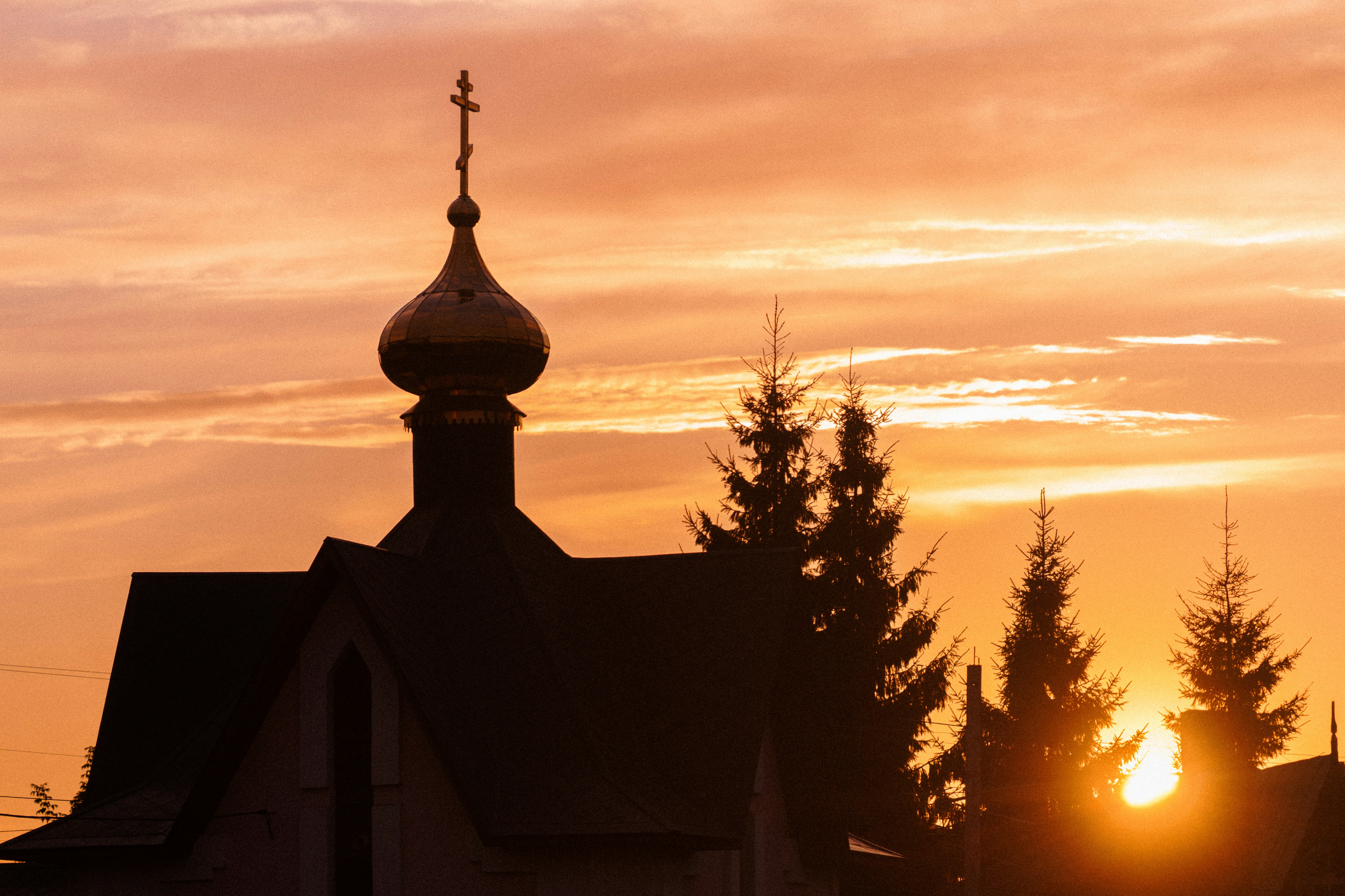 Un dôme d’église orthodoxe avec une croix sur un ciel orange chaud