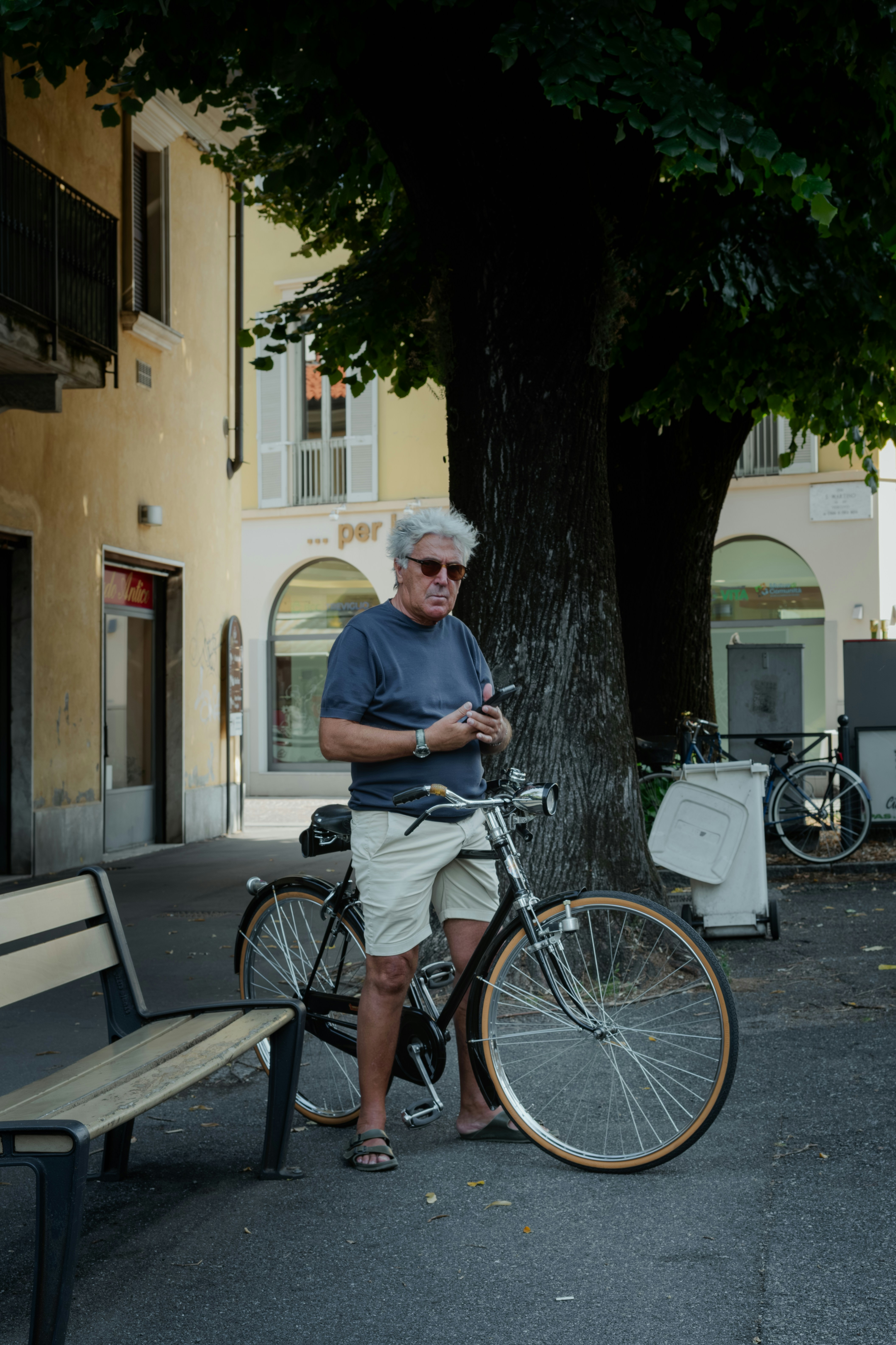 A man with grey hair using a smartphone beside a bicycle on a street