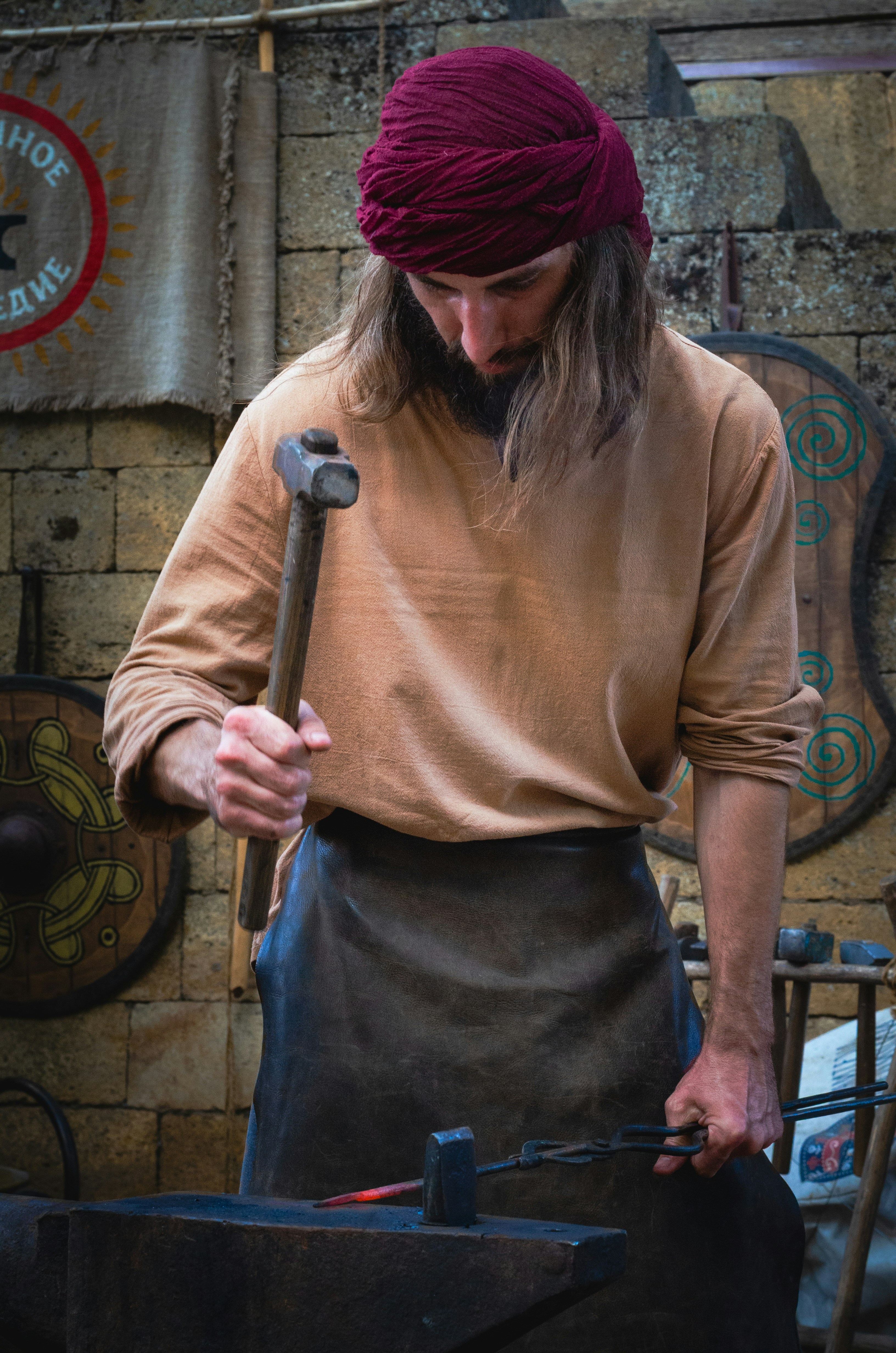 A blacksmith in a maroon turban hammering glowing metal on an anvil