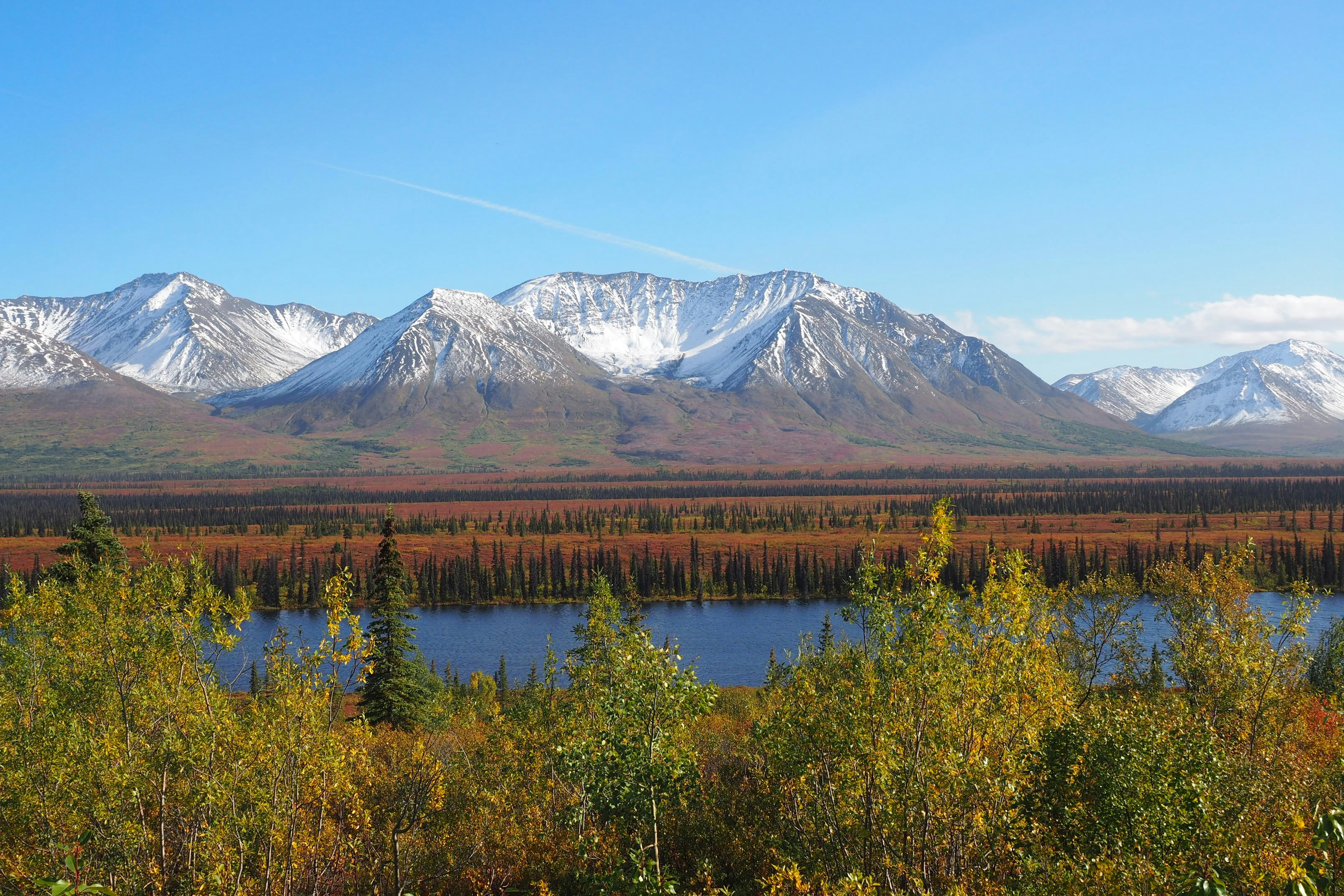 Snow-capped mountains above a dark blue lake and autumn forest under clear sky
