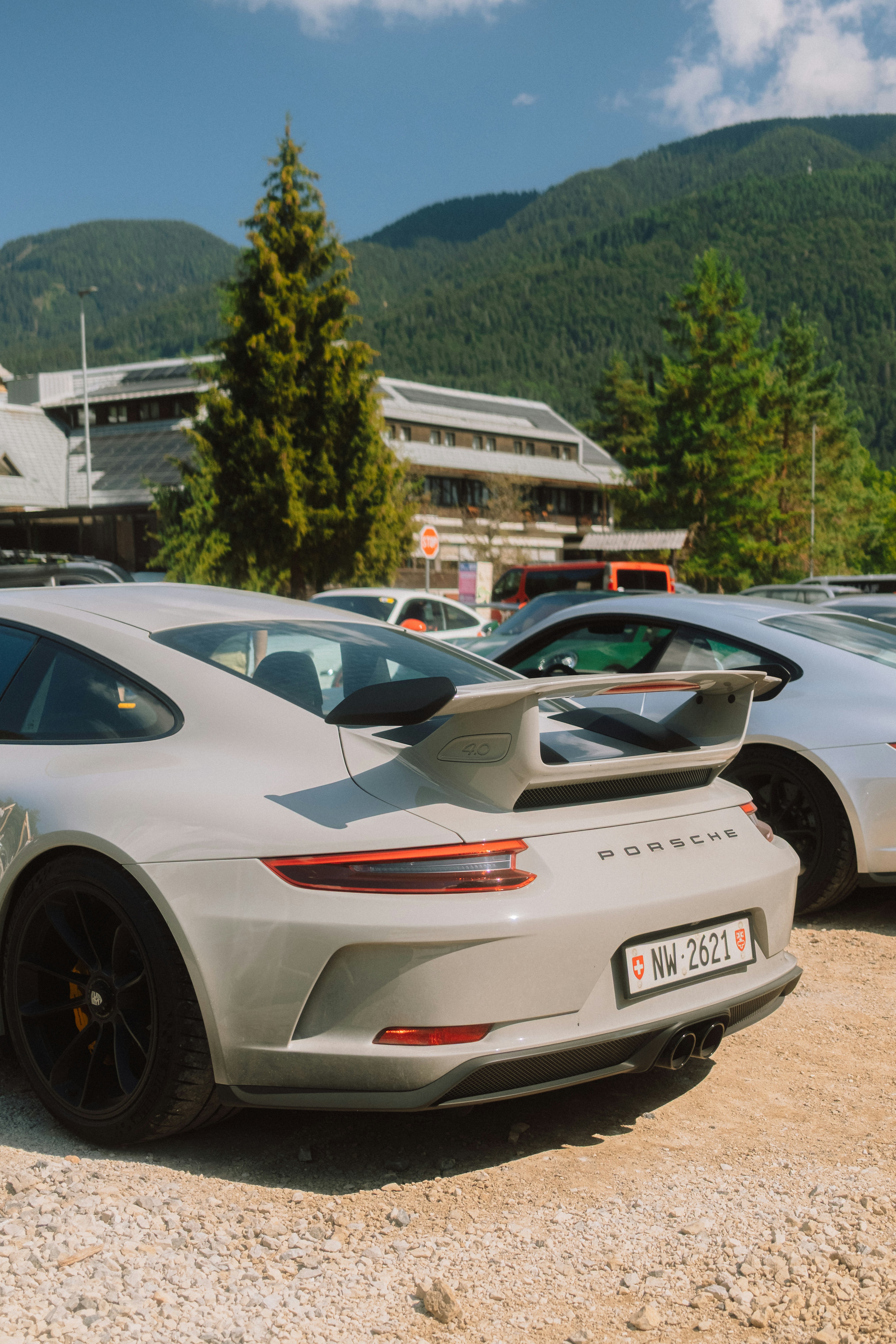 A grey sports car with a rear spoiler parked on a gravel lot