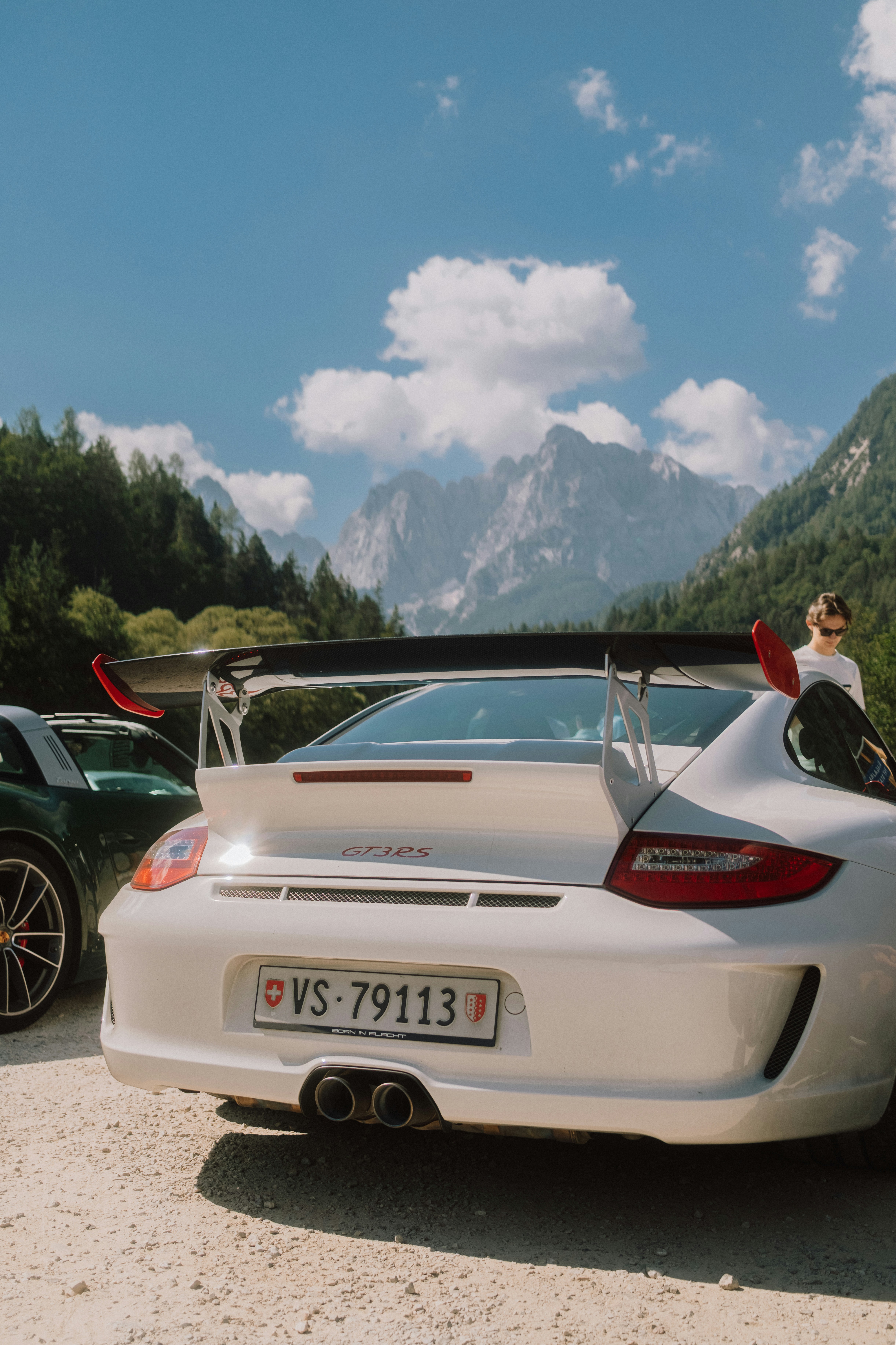 A white Porsche 911 GT3 RS parked on a gravel road before mountain peaks