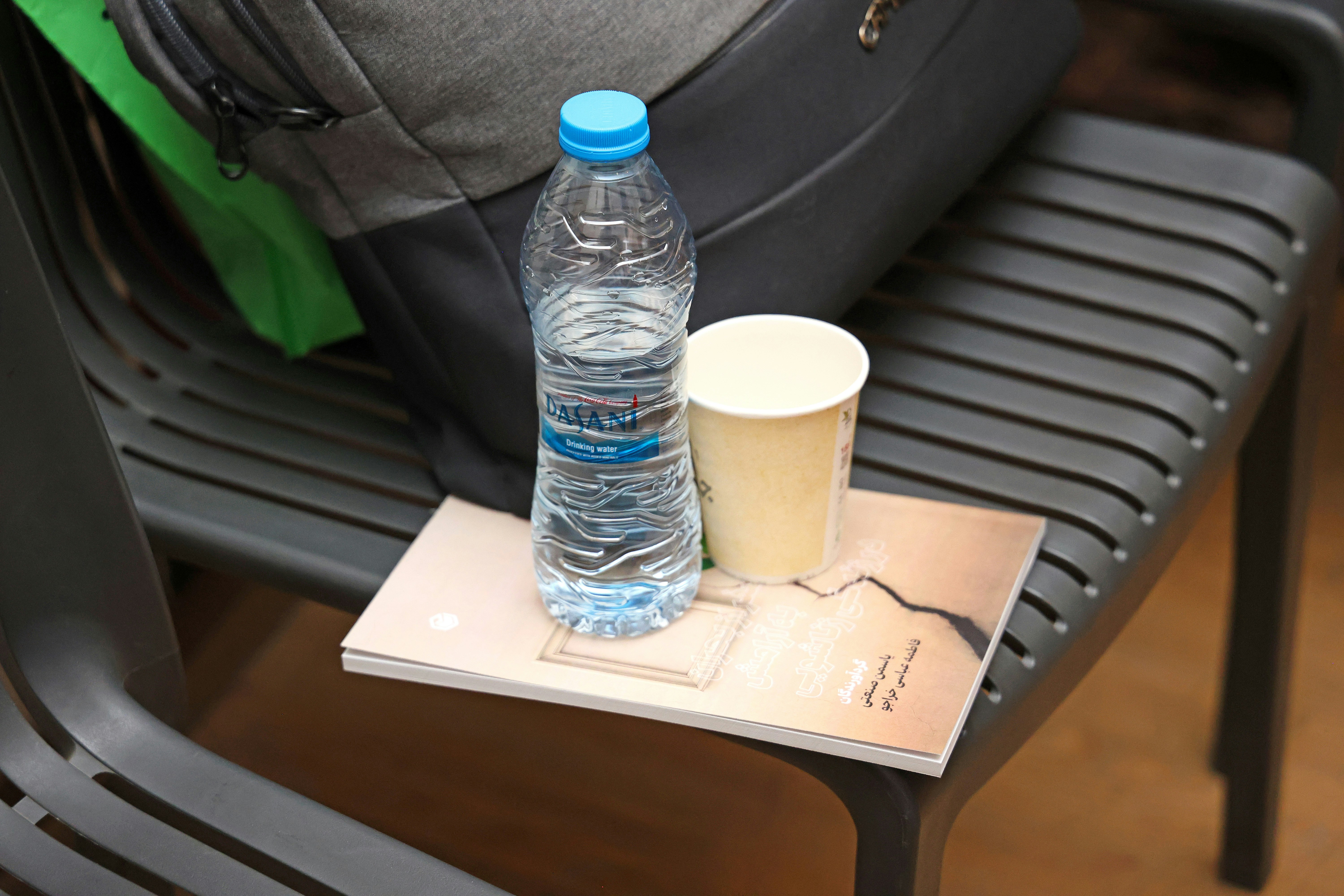 A plastic water bottle and a paper cup on a book on a chair