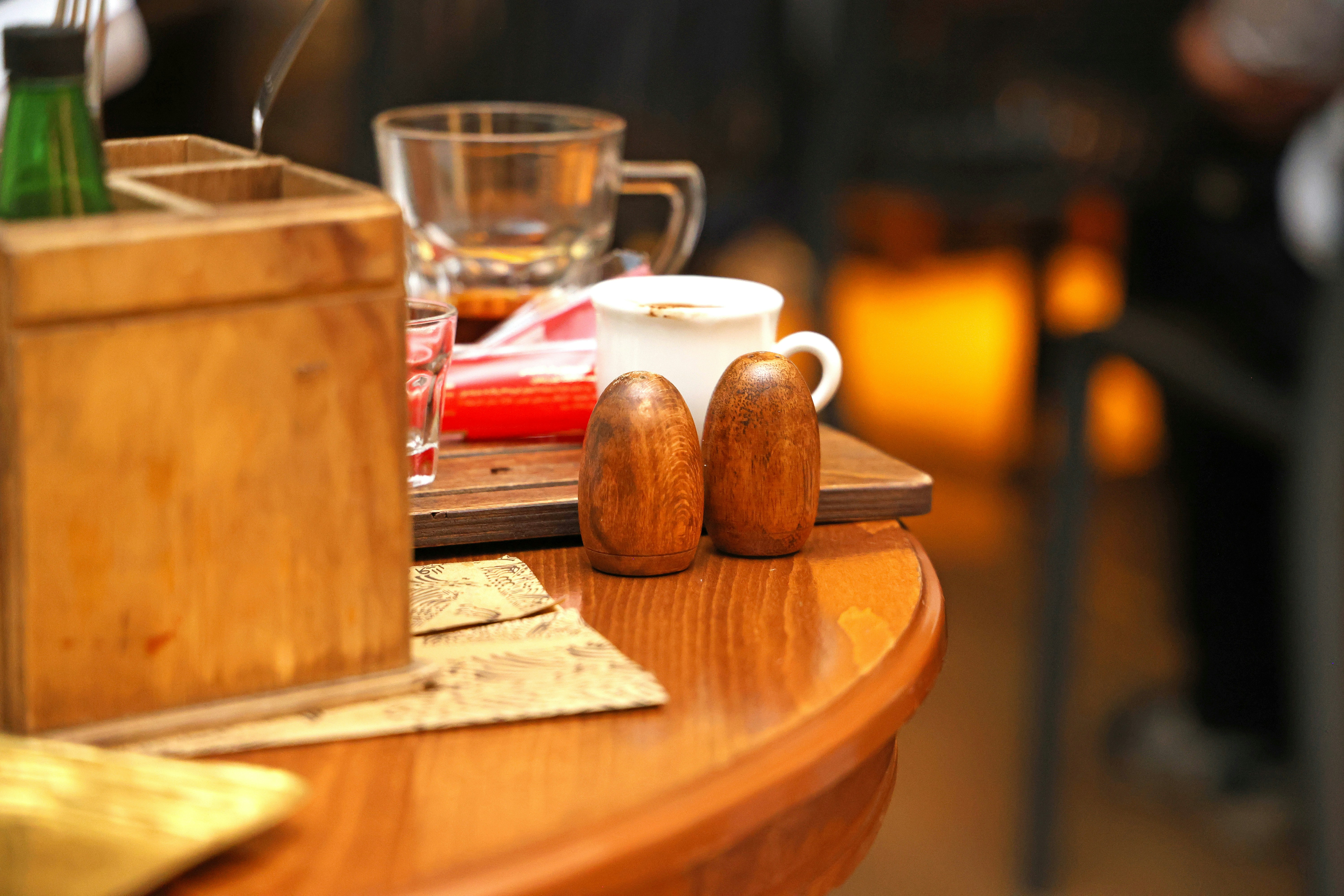 Two wooden salt and pepper shakers on a round wooden table in a cafe
