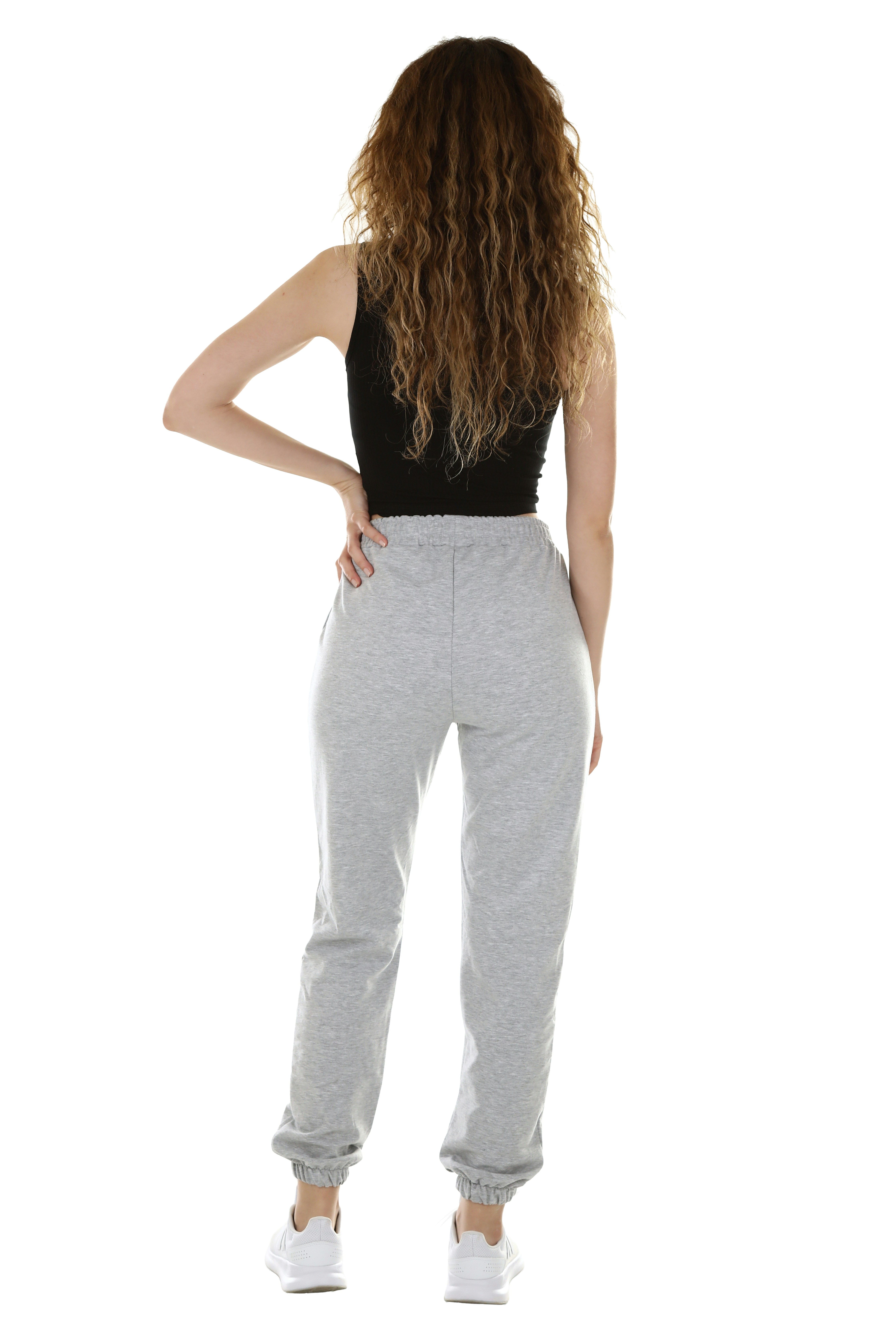 A woman with long curly hair in a black tank top and grey sweatpants