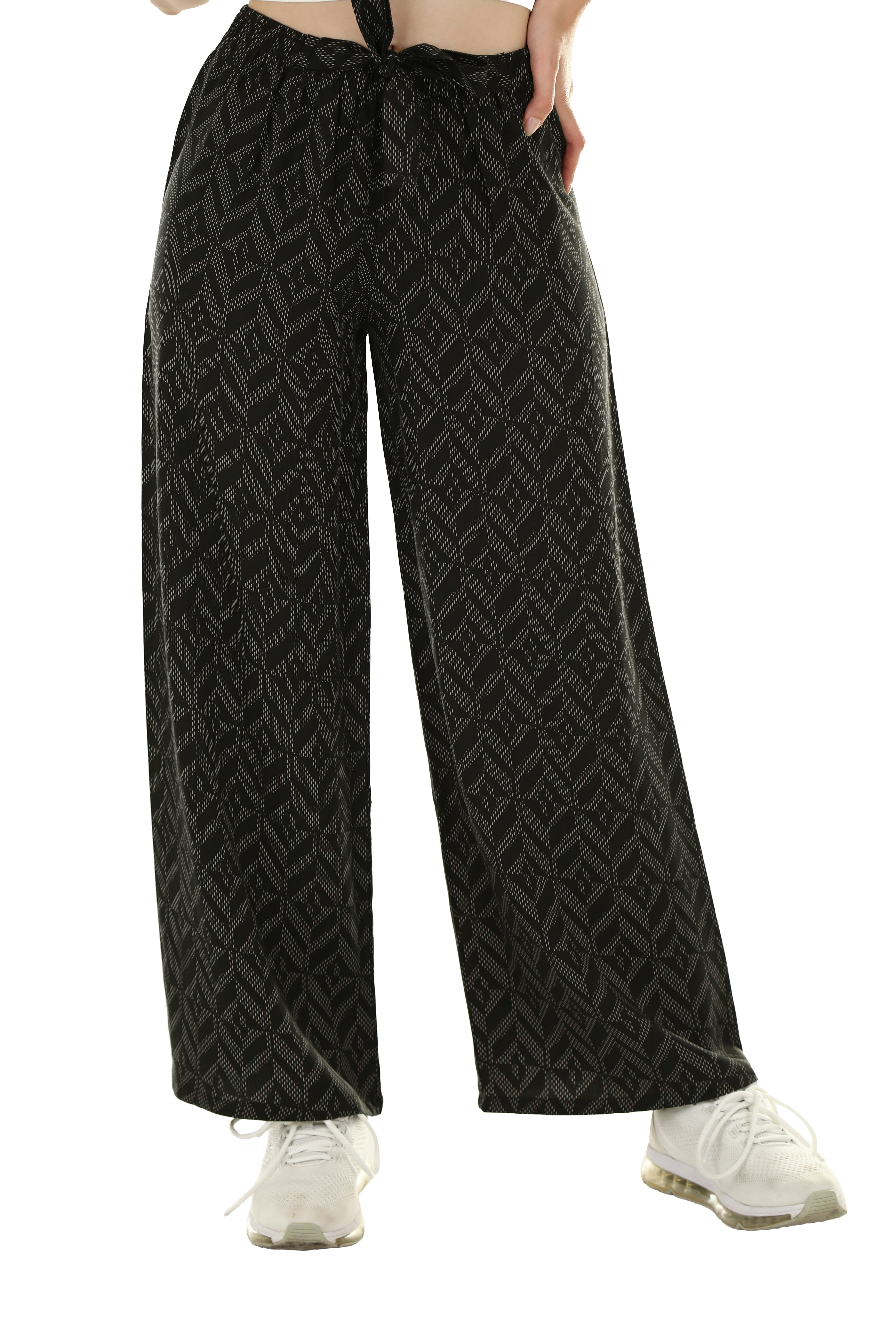 A person wearing wide-leg black trousers with a white geometric pattern and white sneakers