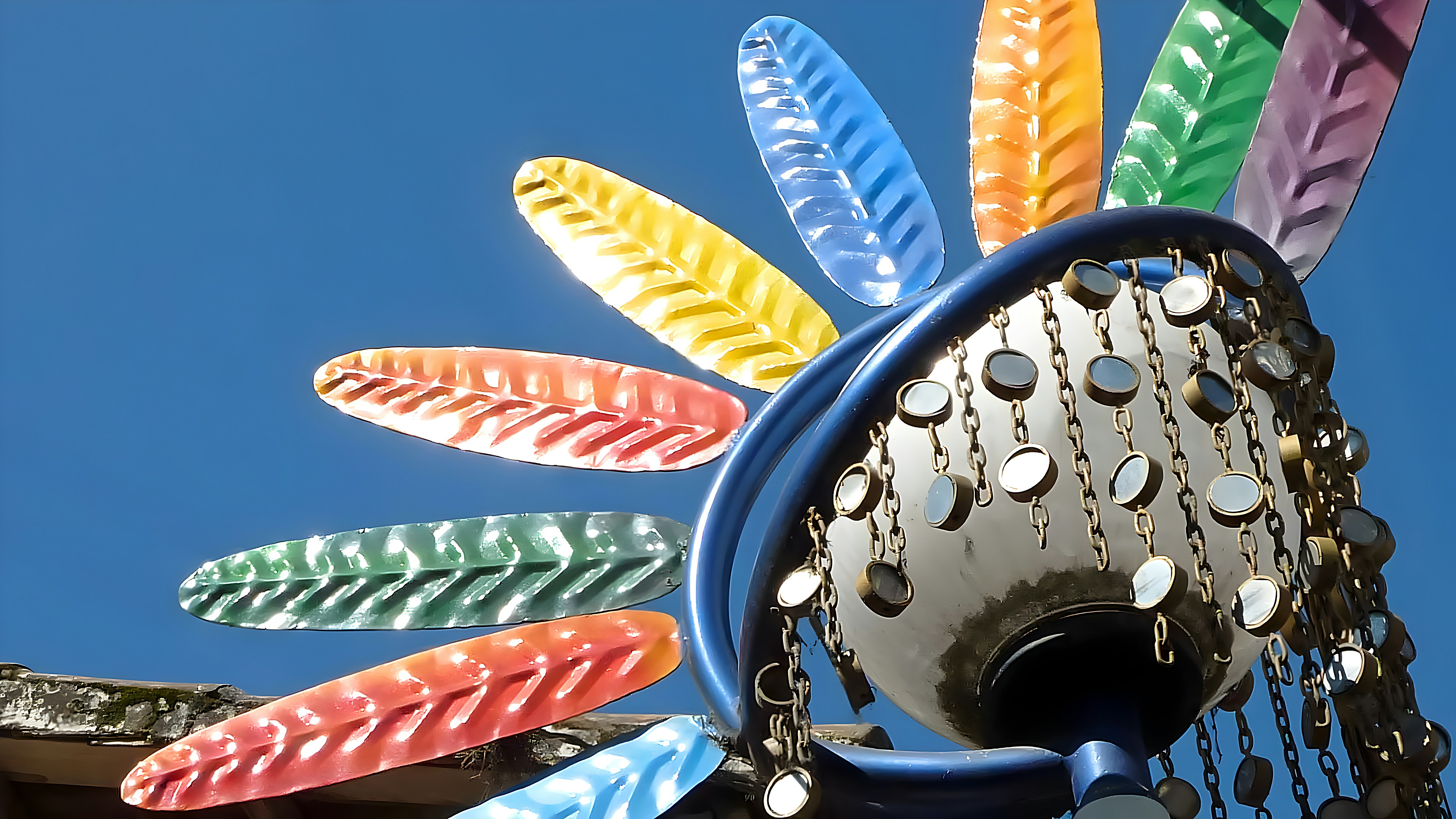 A decorative lamp with colorful metal feathers against a clear blue sky