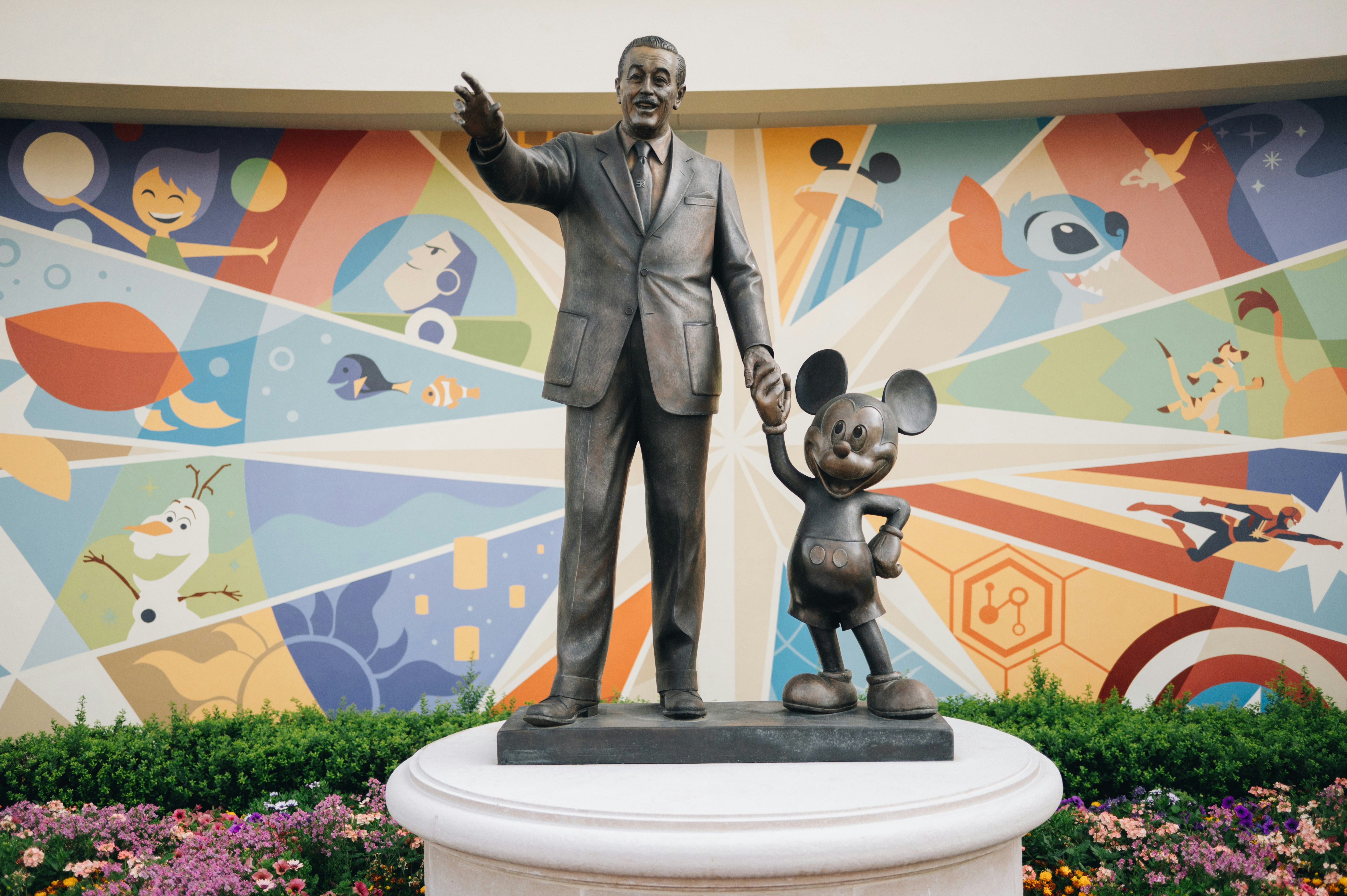 Bronze statue of a man holding hands with a mouse before a colorful mural