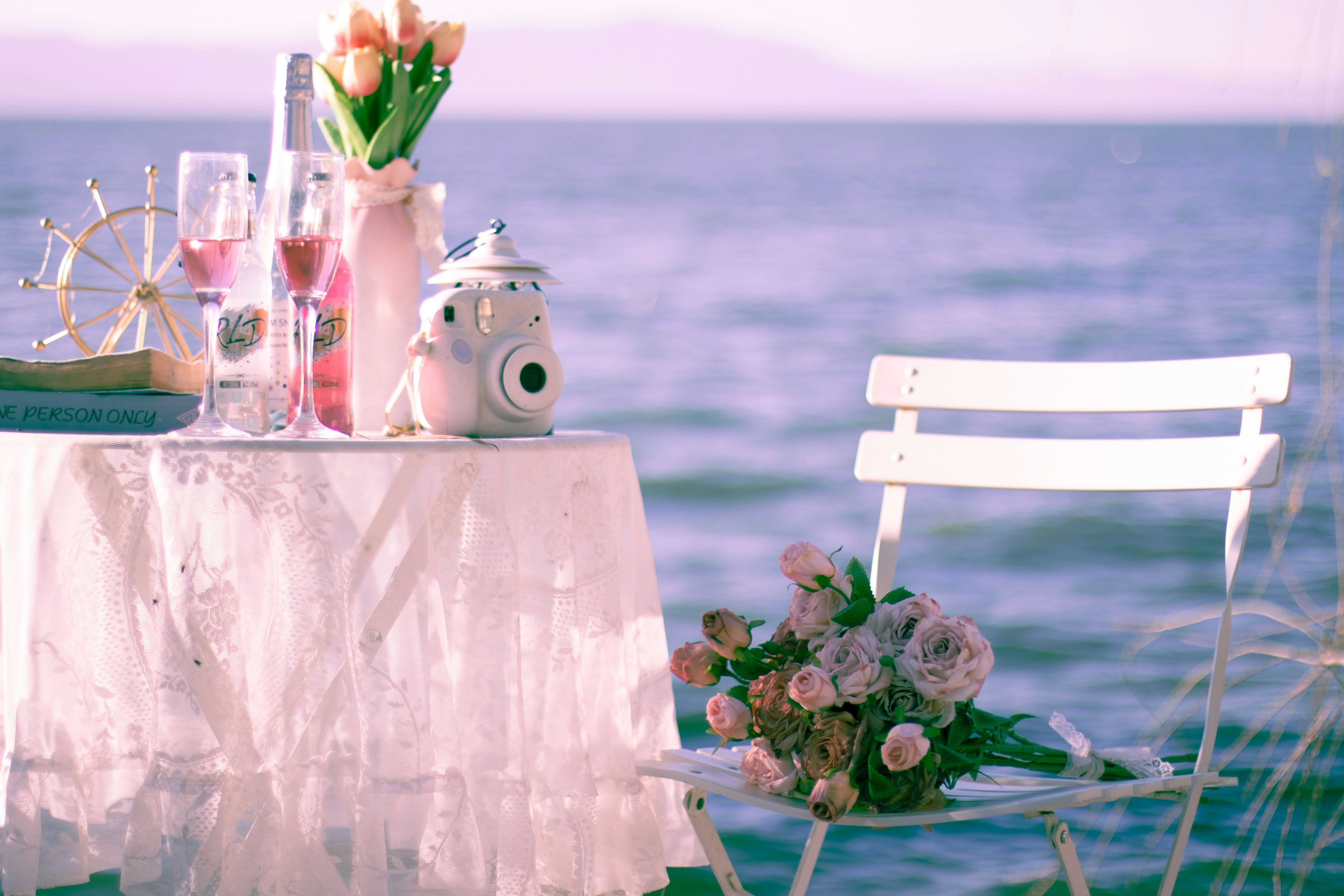 A table with lace cloth, pink drinks, and flowers beside a white chair