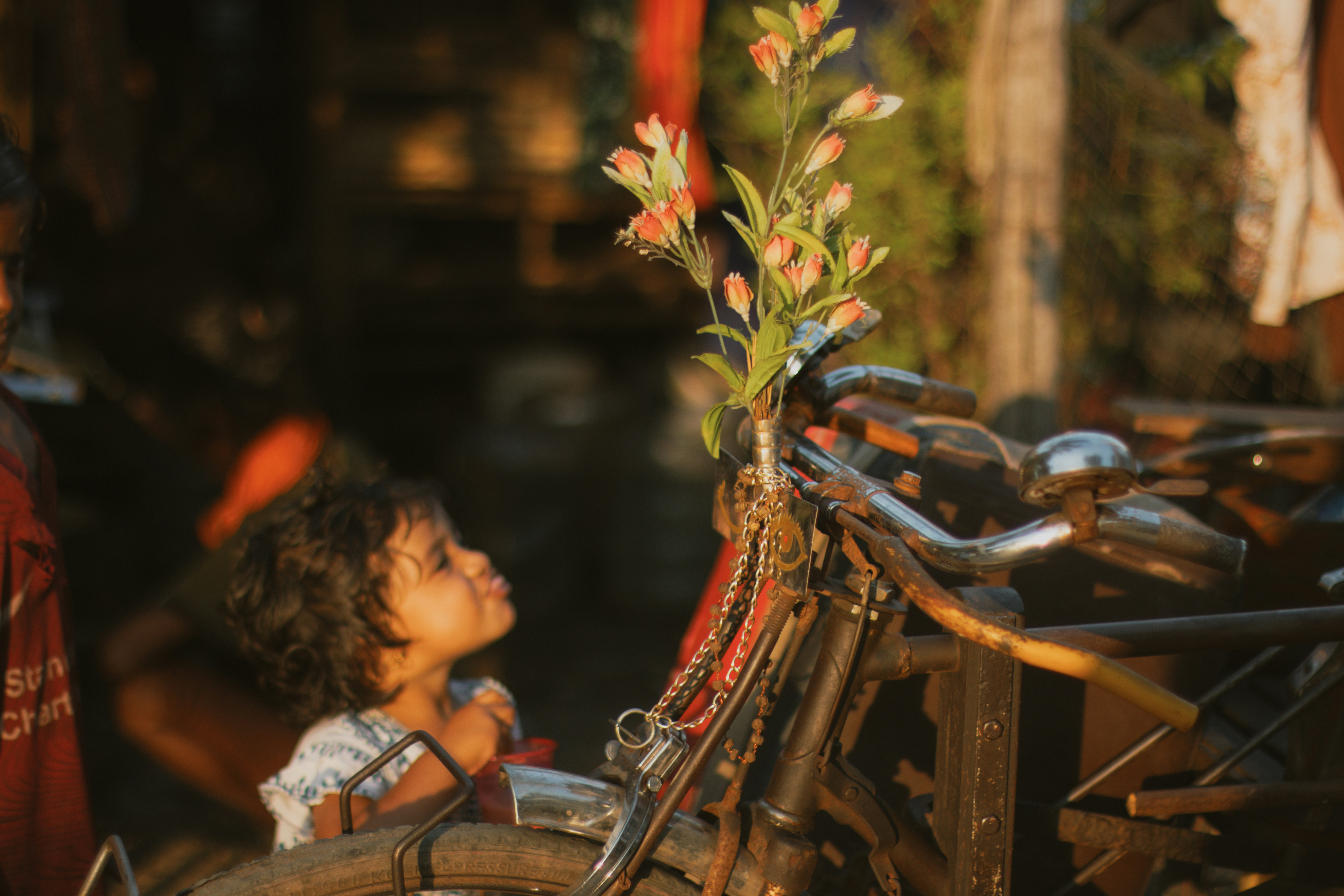 A child looking at a bicycle decorated with orange flowers in golden light