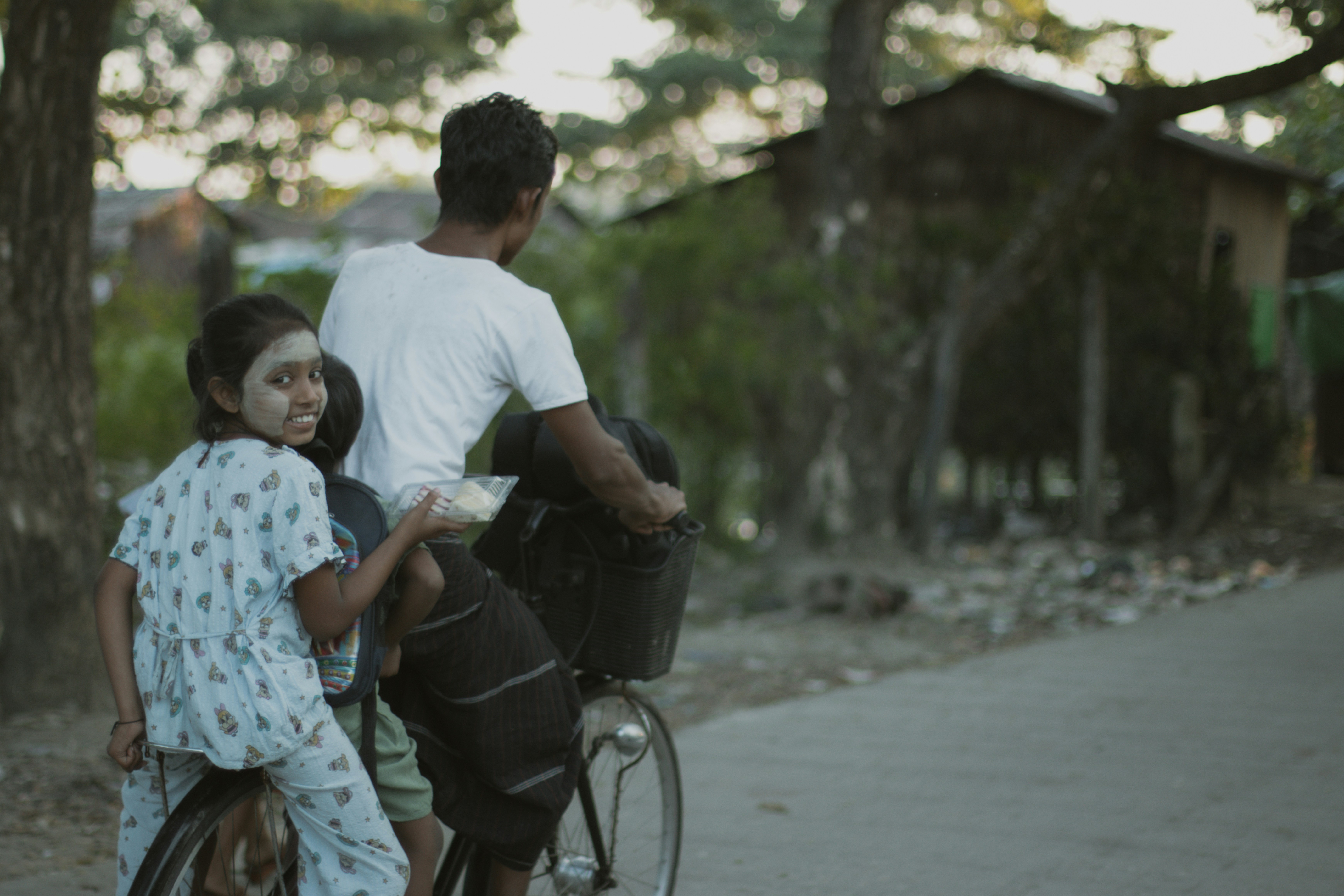 A man cycling with two children on a bicycle along a rural road