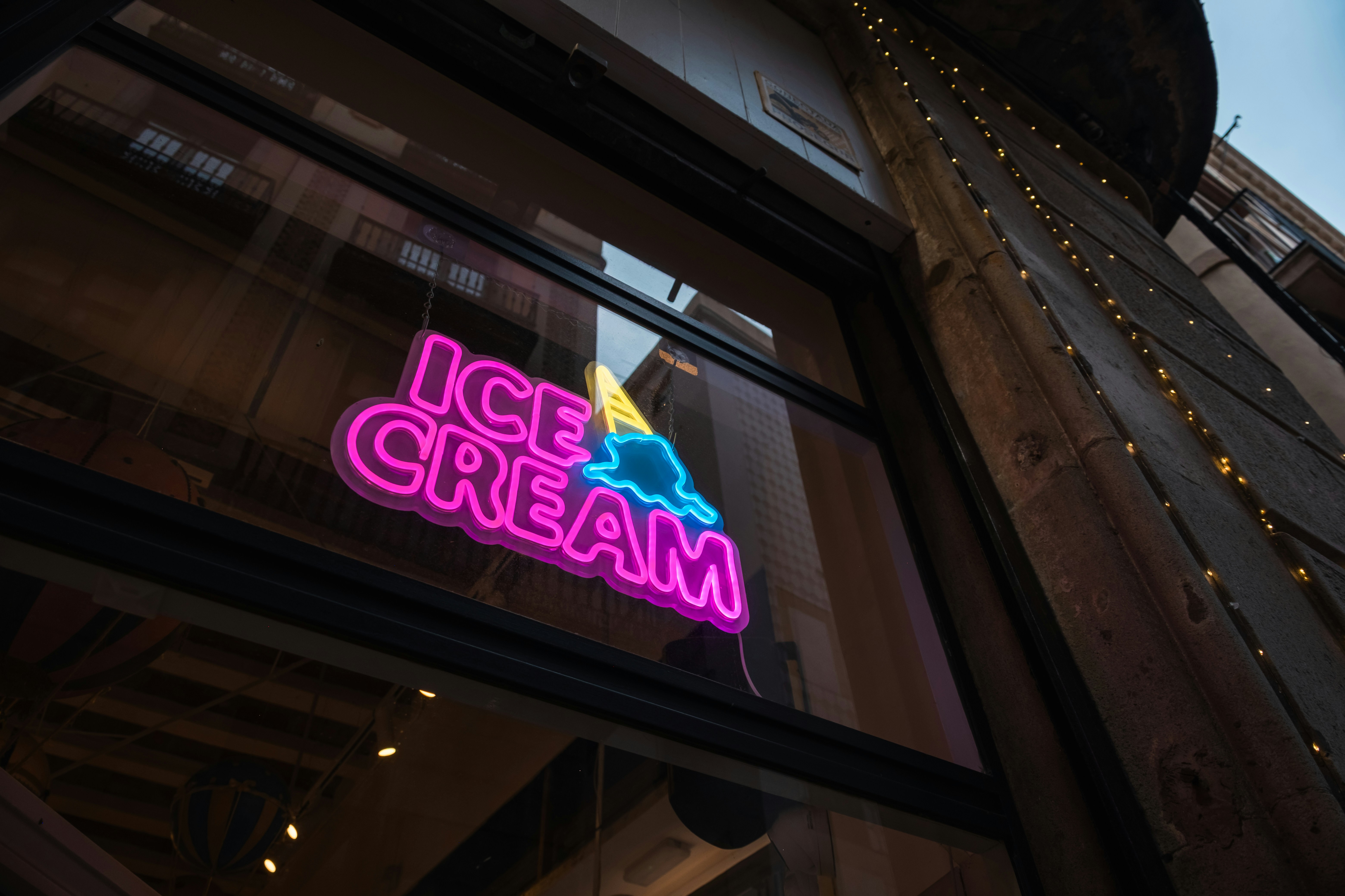 A pink and blue neon sign reading ICE CREAM in a shop window