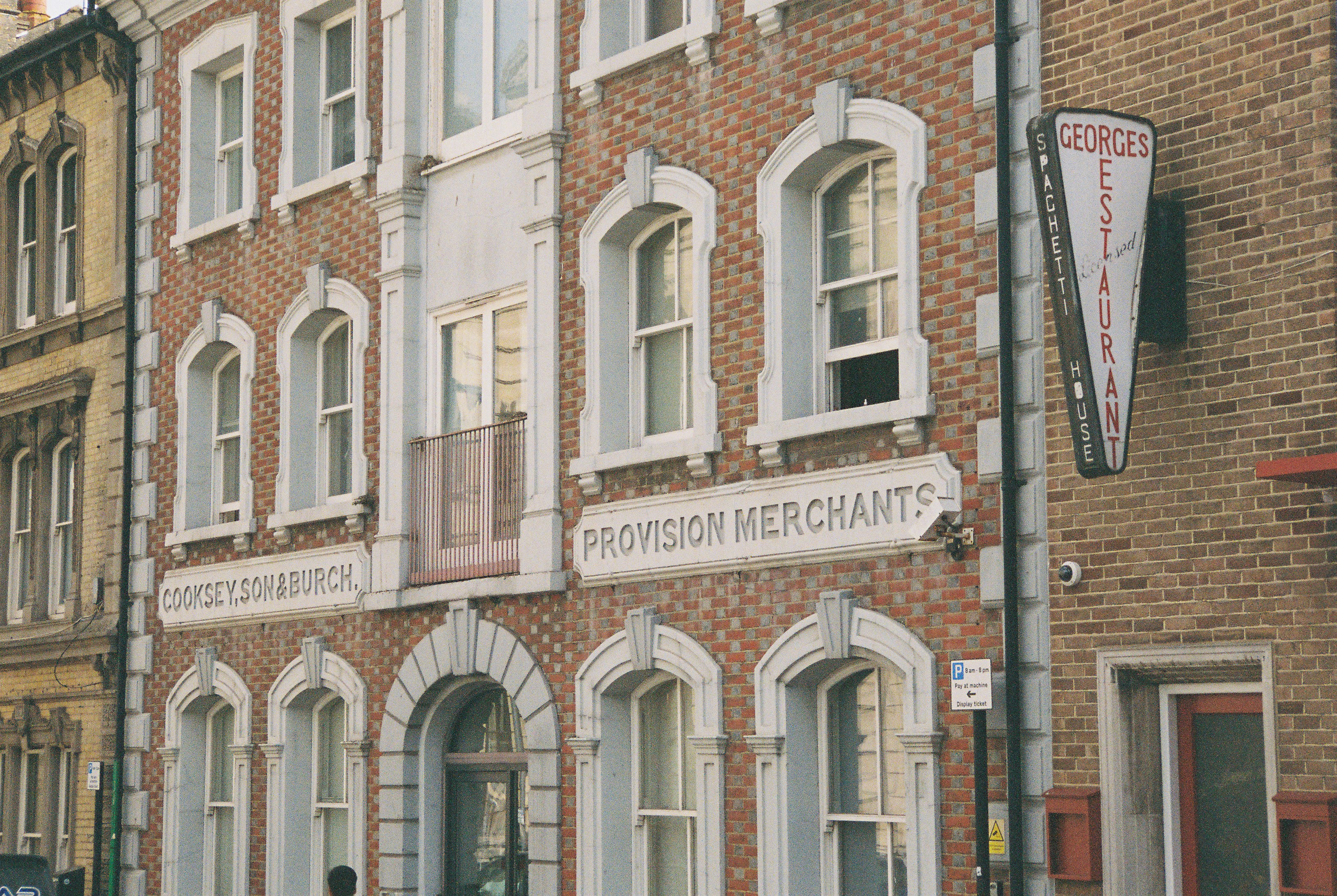 A brick storefront with white arched windows and carved signs reading "PROVISION MERCHANTS"