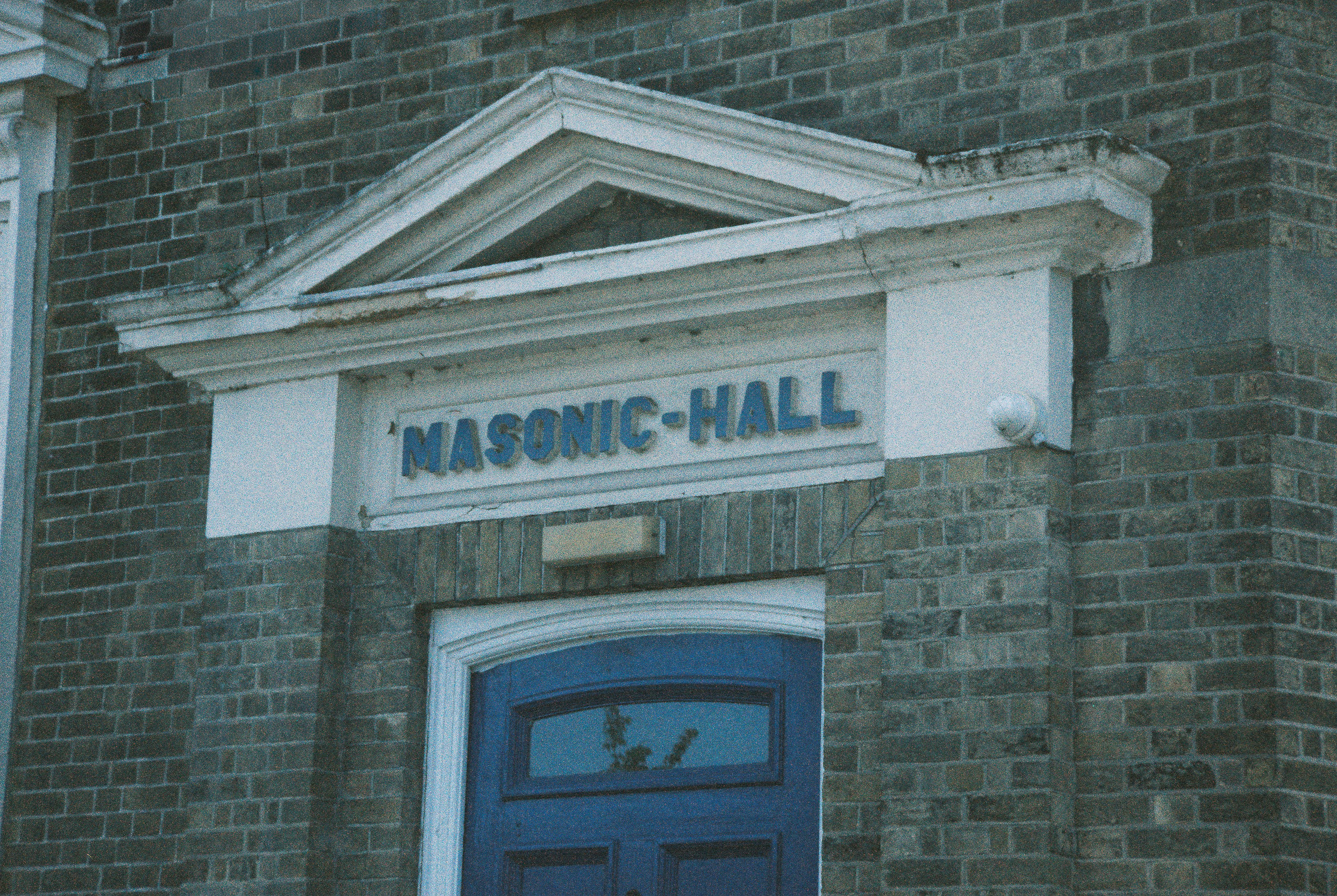 A blue door beneath a pediment with a sign reading MASONIC-HALL on brick