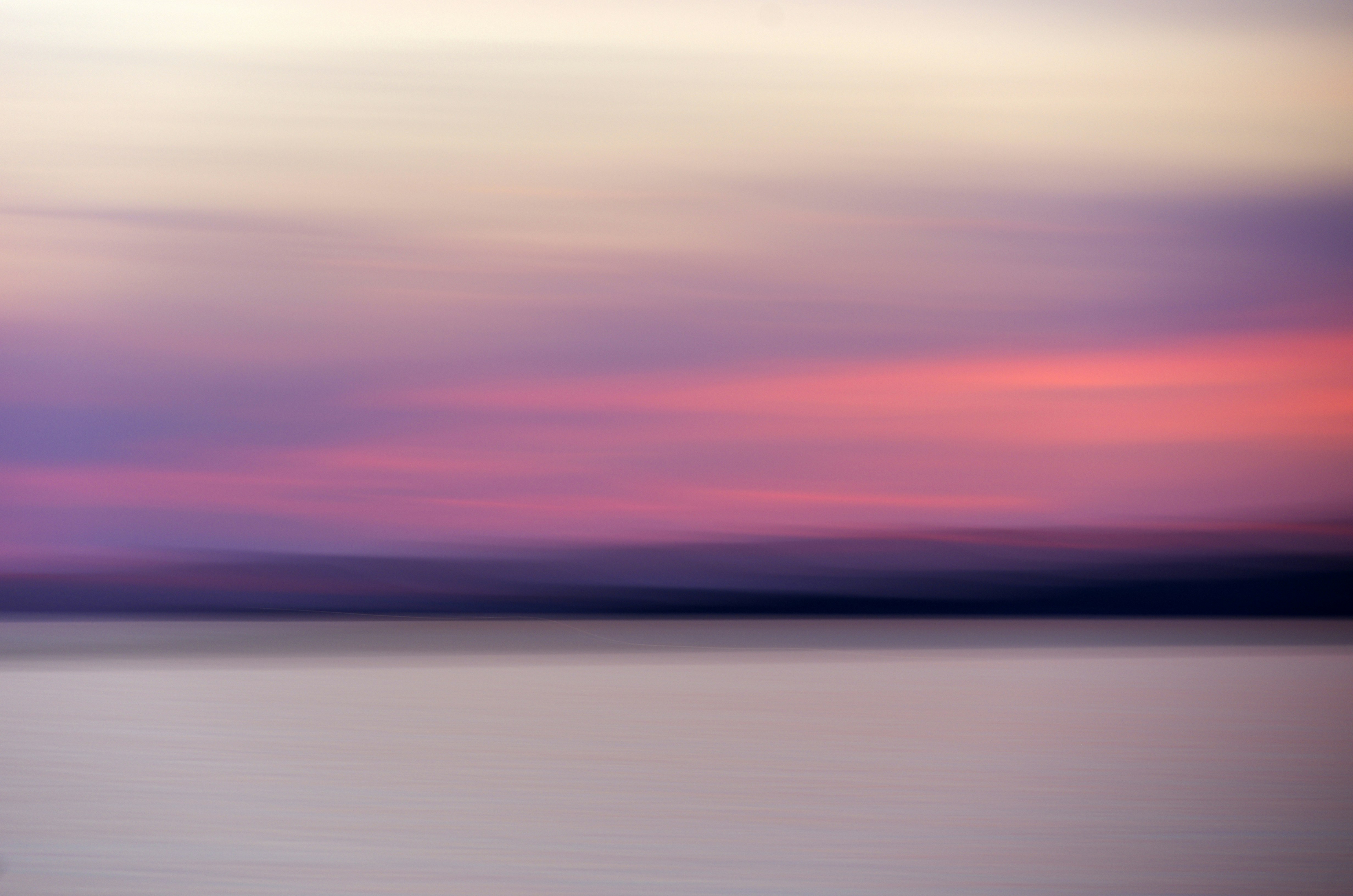 A motion blur of pink and purple clouds above a calm water surface