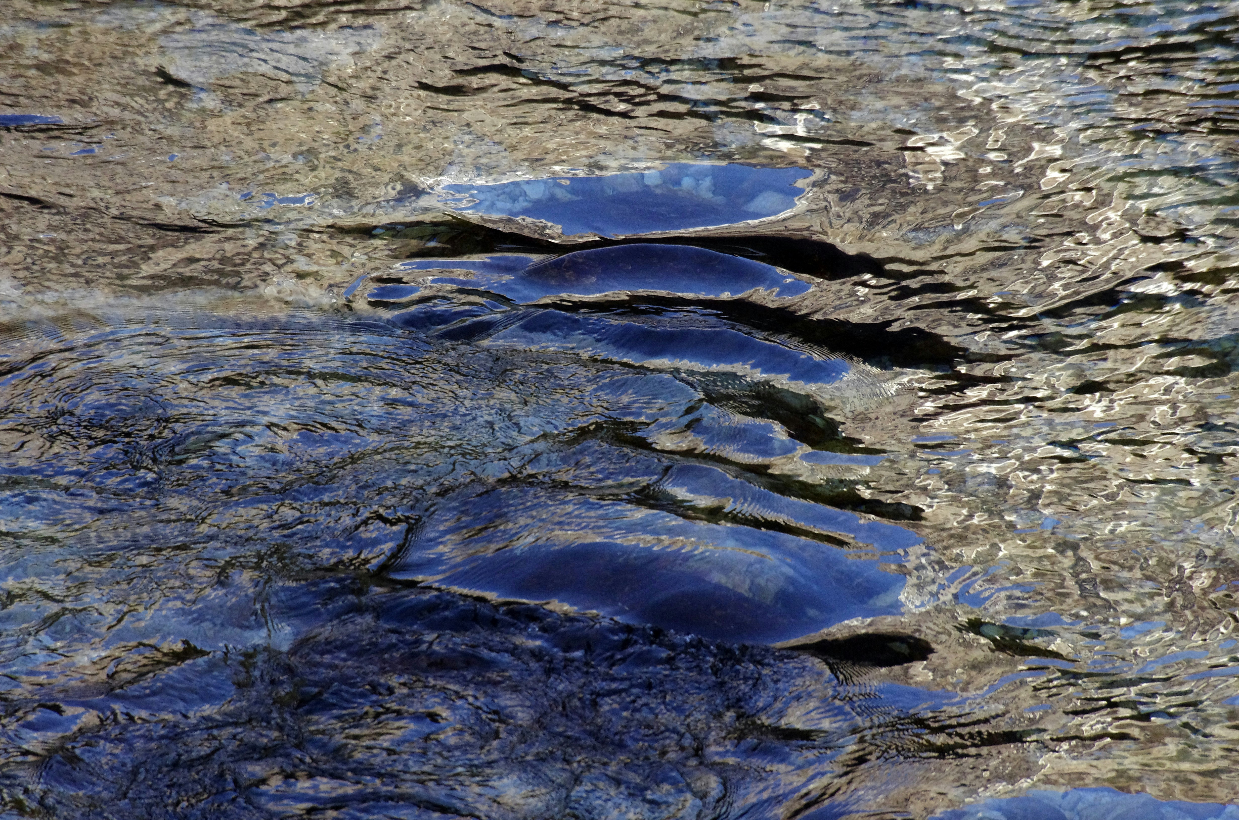 Dark blue water flowing over smooth submerged rocks in a shallow stream