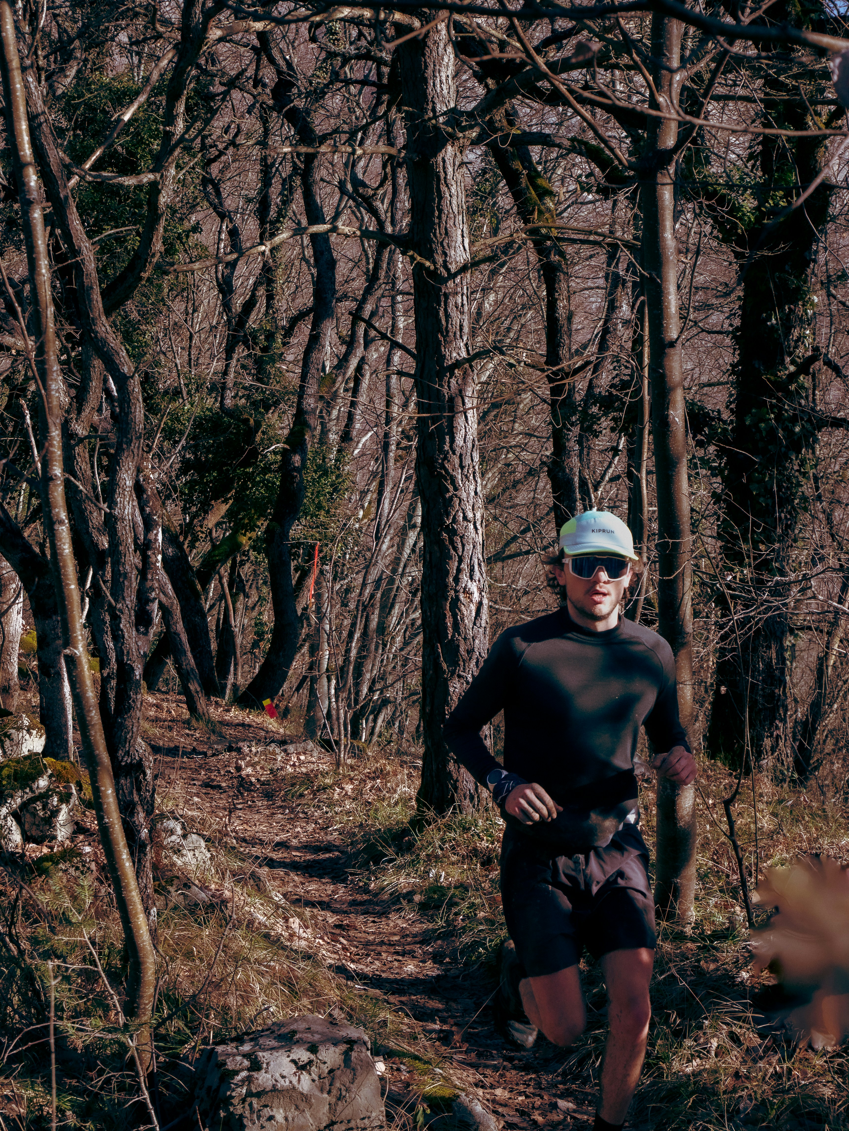 A man running on a narrow dirt trail through a dense forest