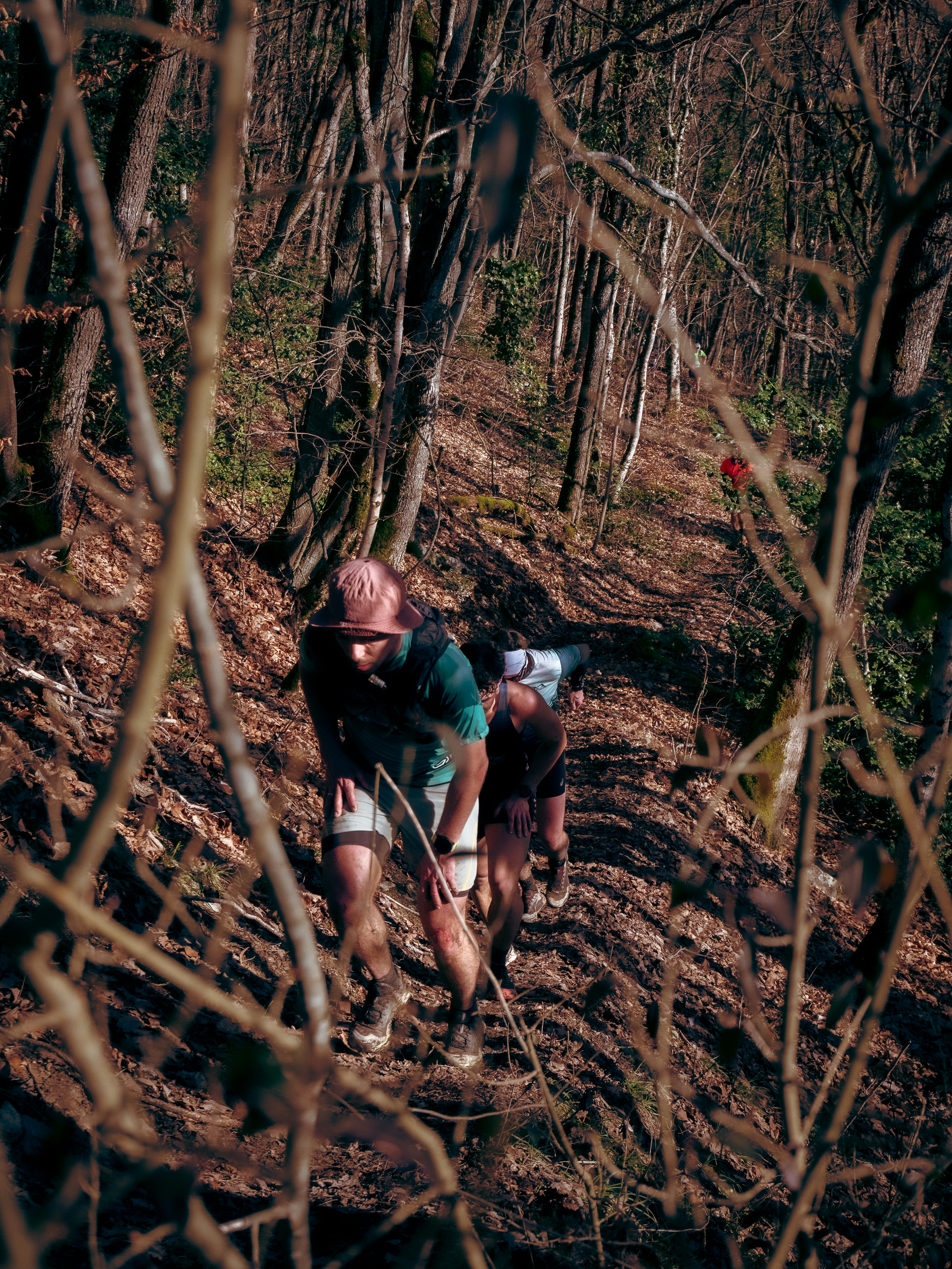 Three people running up a steep forest trail covered in dry brown leaves