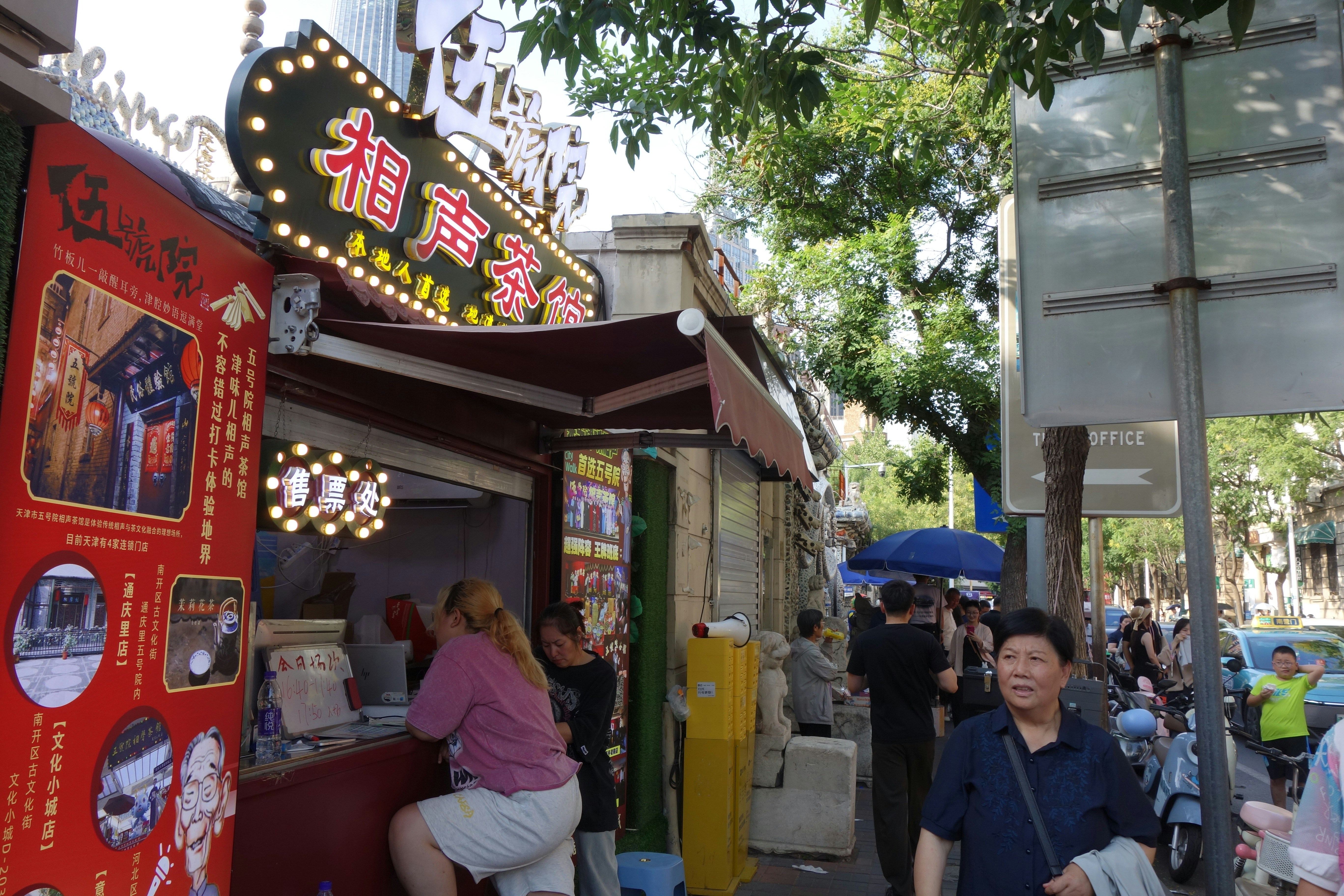 A street scene with a ticket booth and people walking on a sidewalk