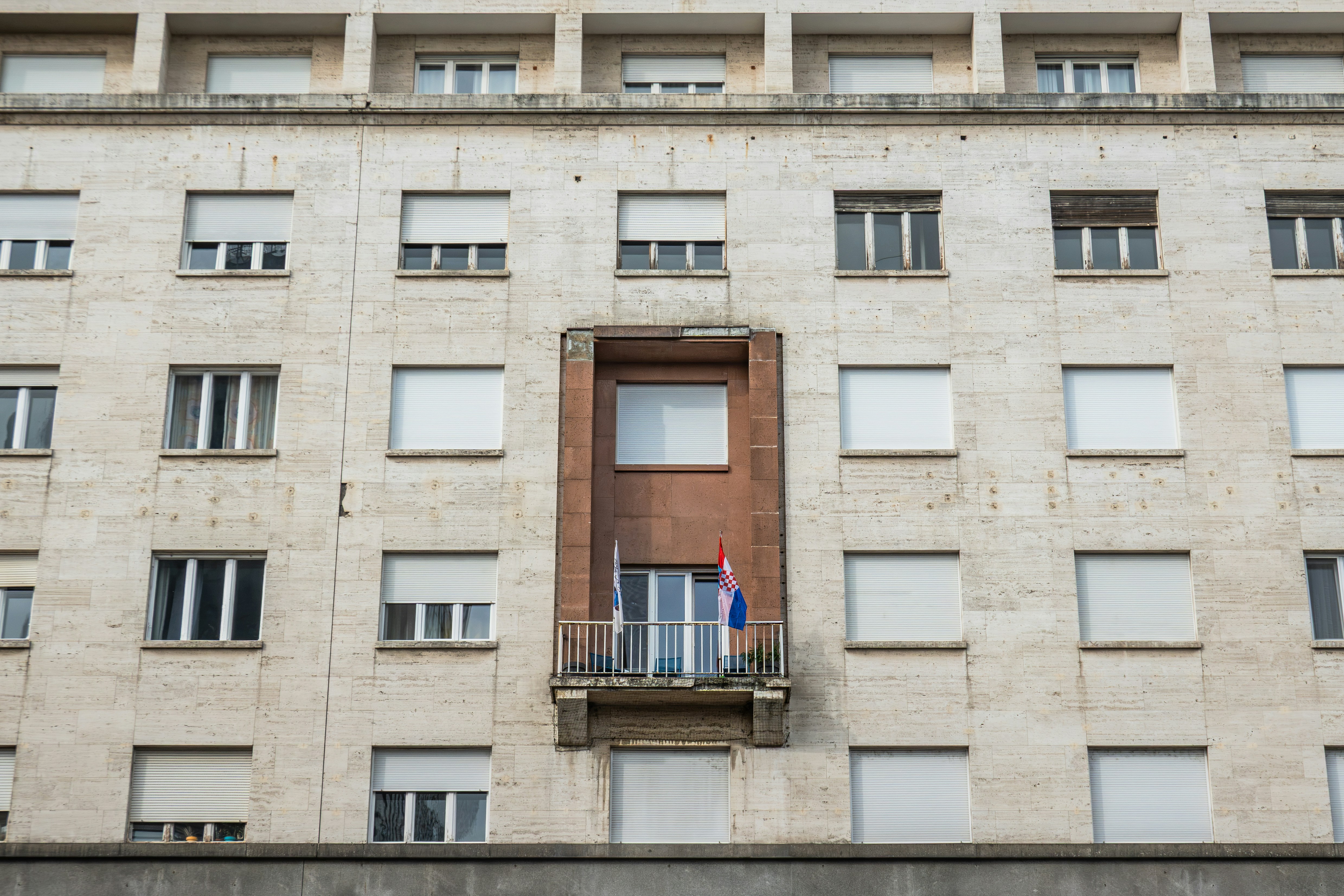 A stone building facade with rows of windows and a central balcony with flags