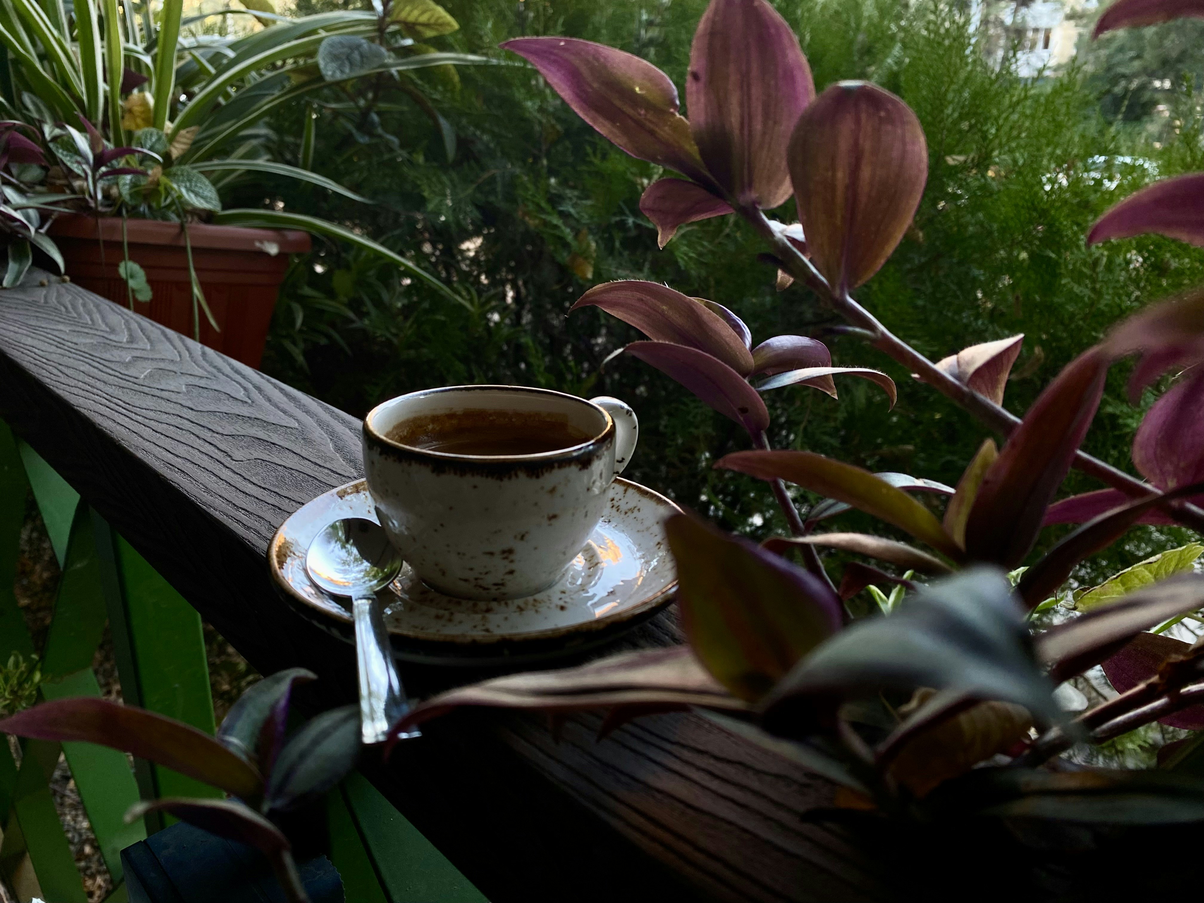 Une tasse de café sur une soucoupe avec une cuillère posée sur une rambarde en bois