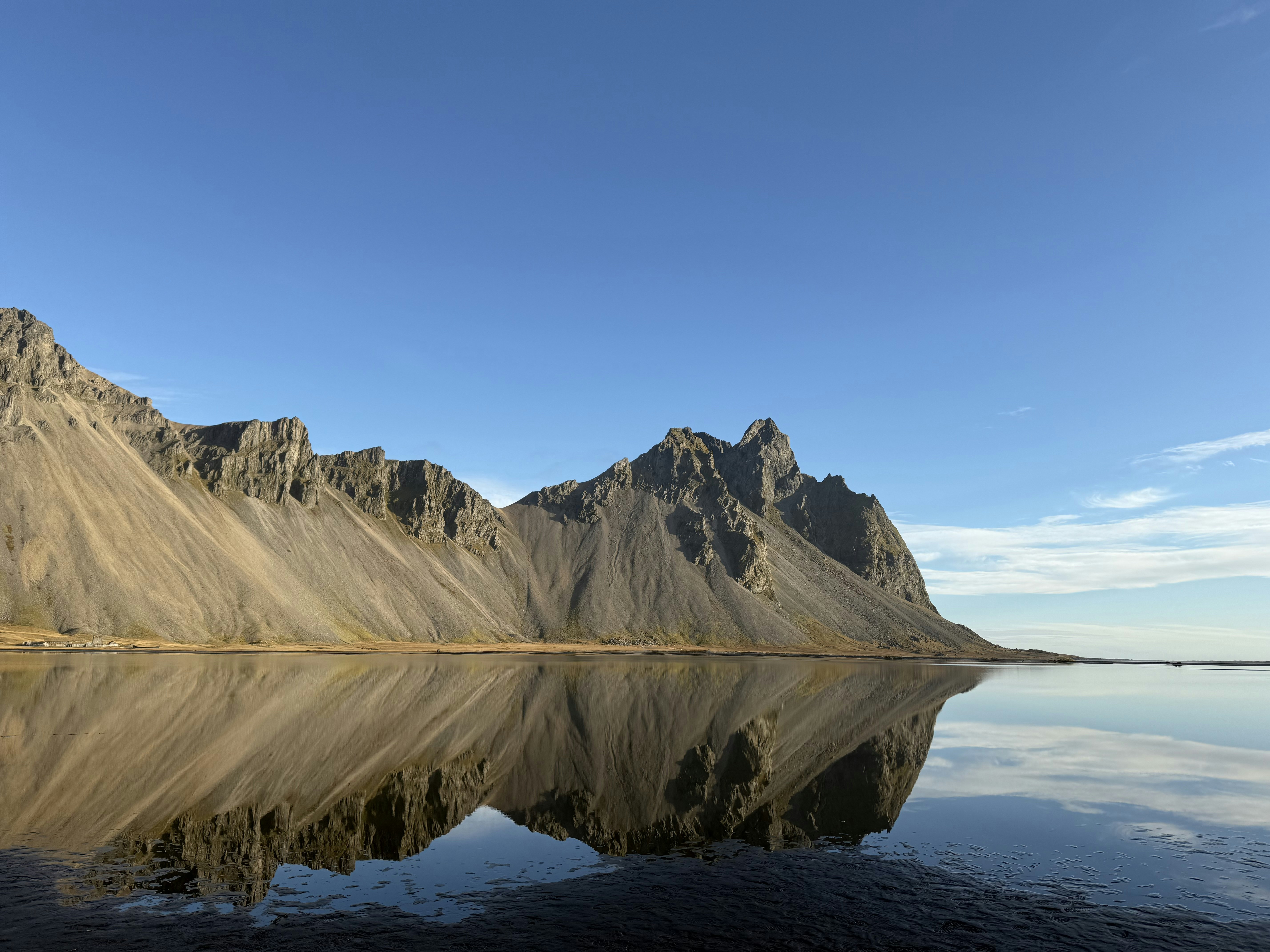 Jagged mountains reflecting in the calm water of a lagoon under a clear sky
