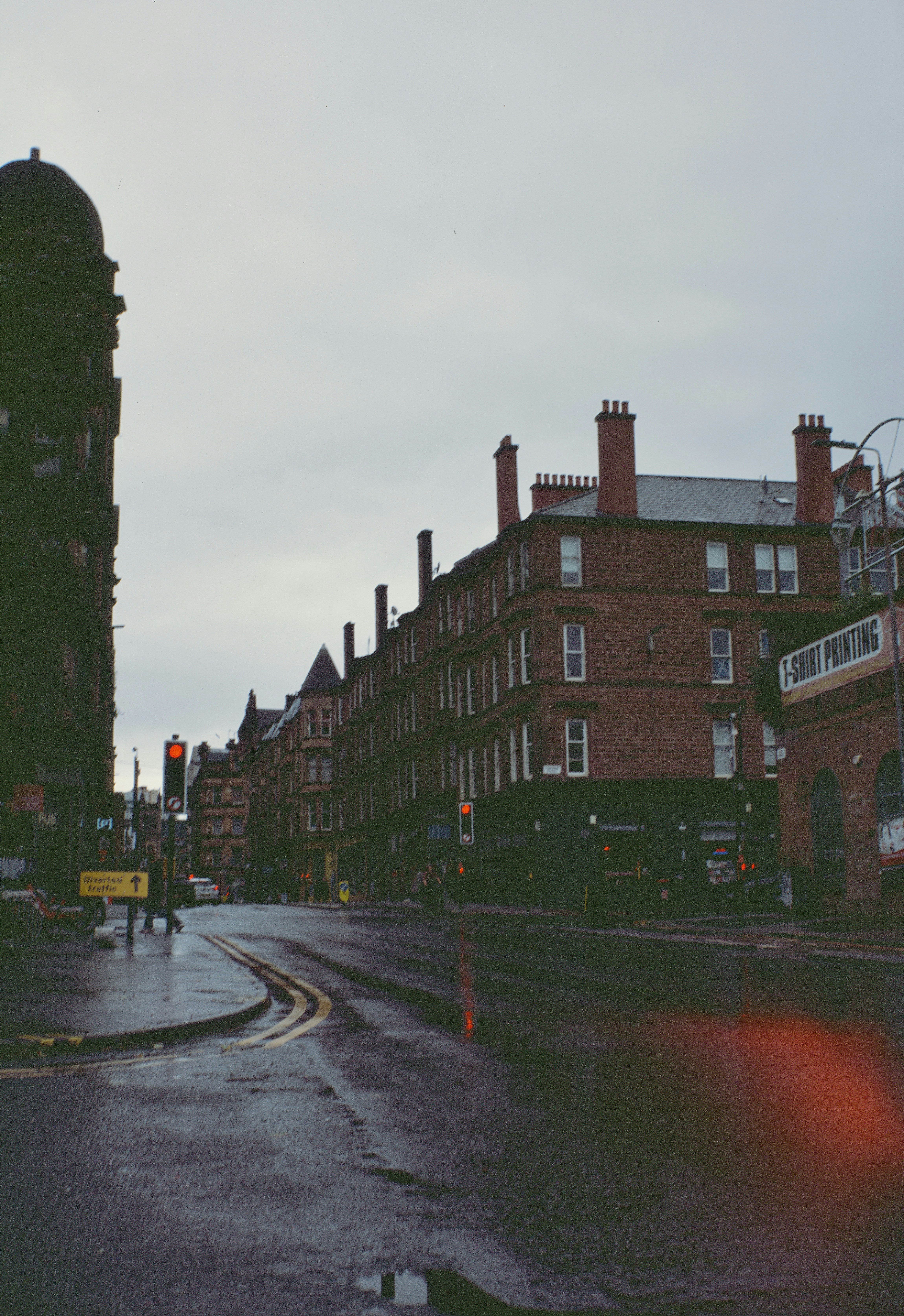 A wet city street with red brick buildings in Glasgow under an overcast sky