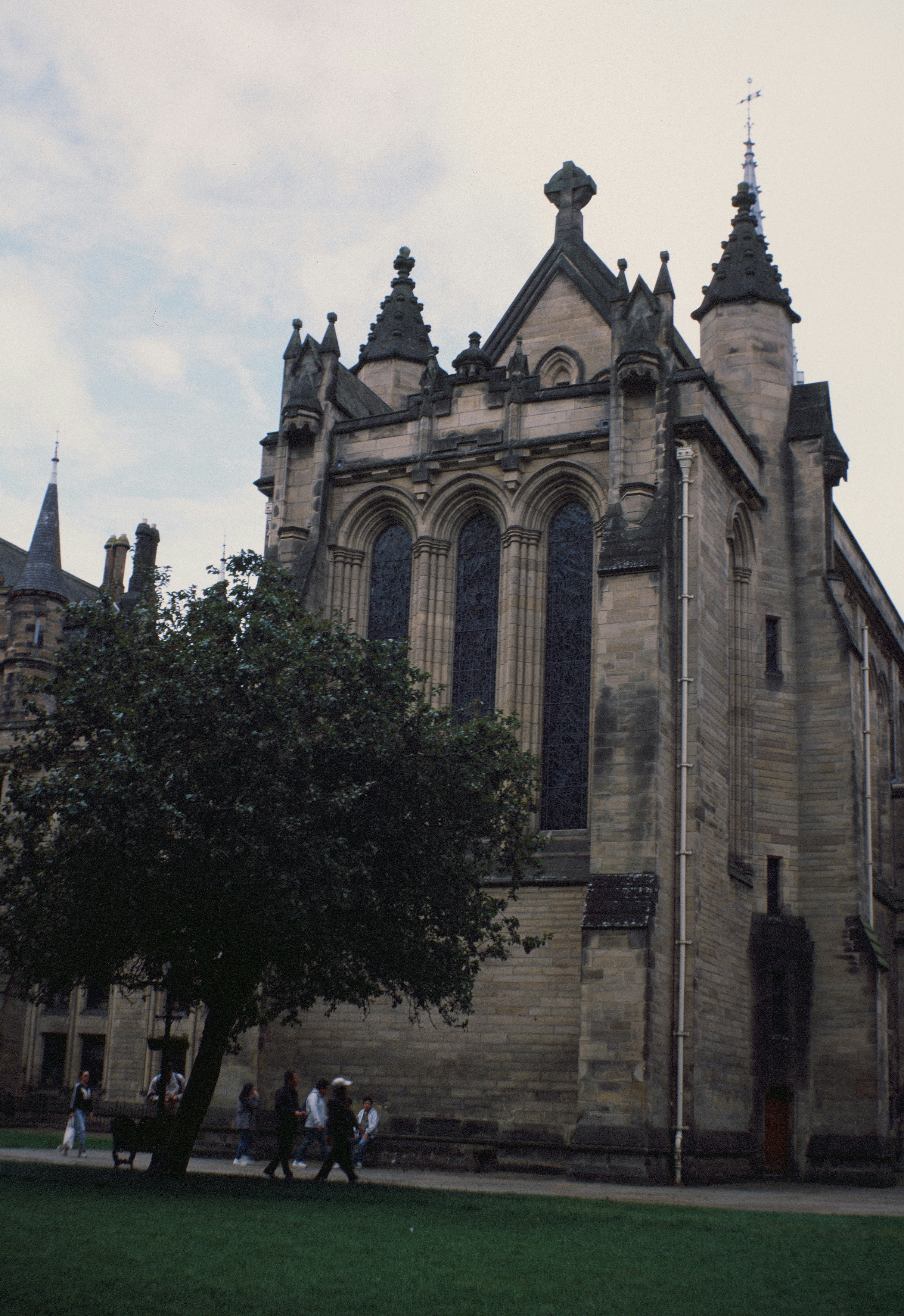 People walking past a stone gothic building with tall arched windows in Glasgow