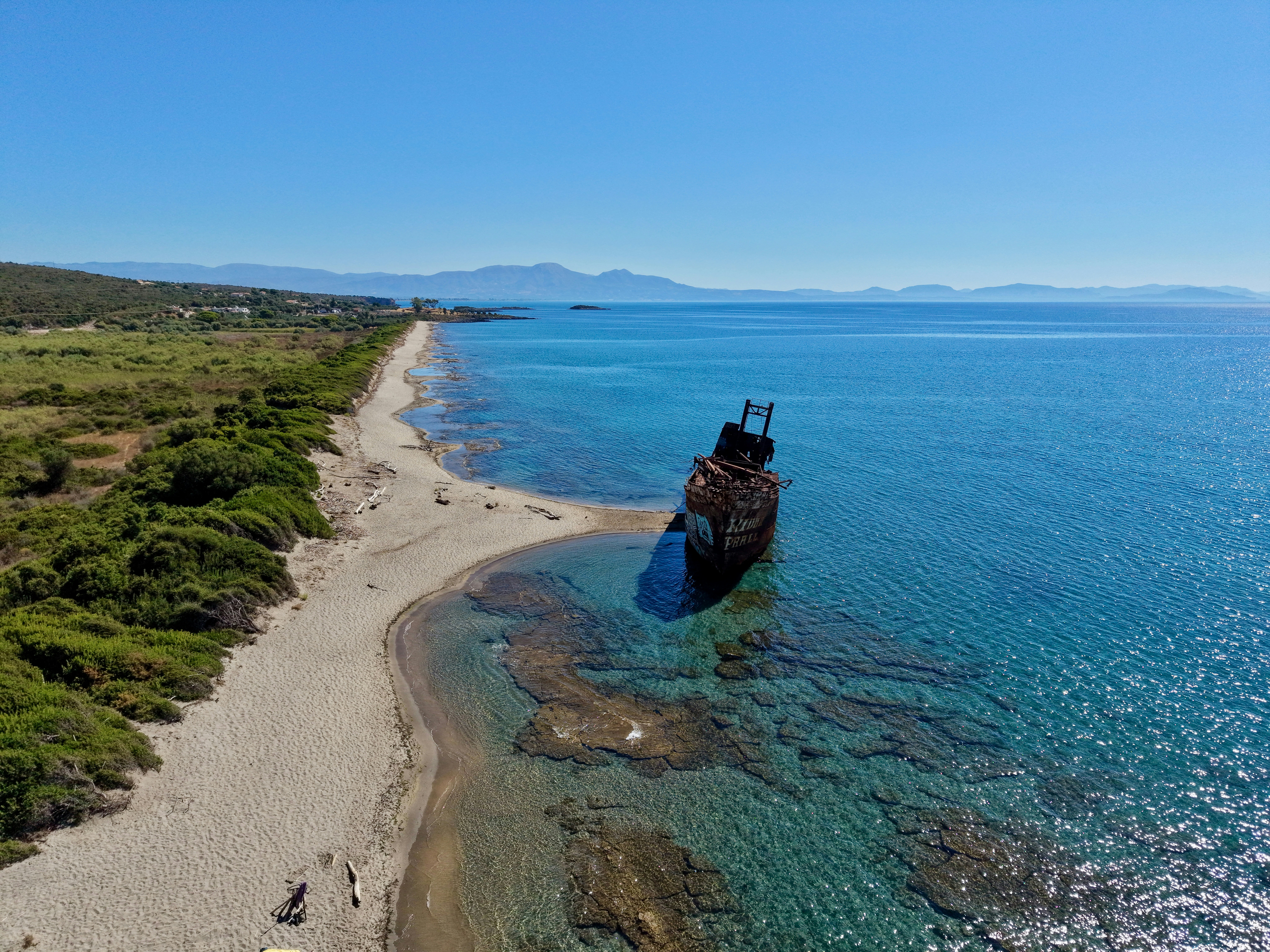An aerial view of a rusted shipwreck beached on a sandy shore